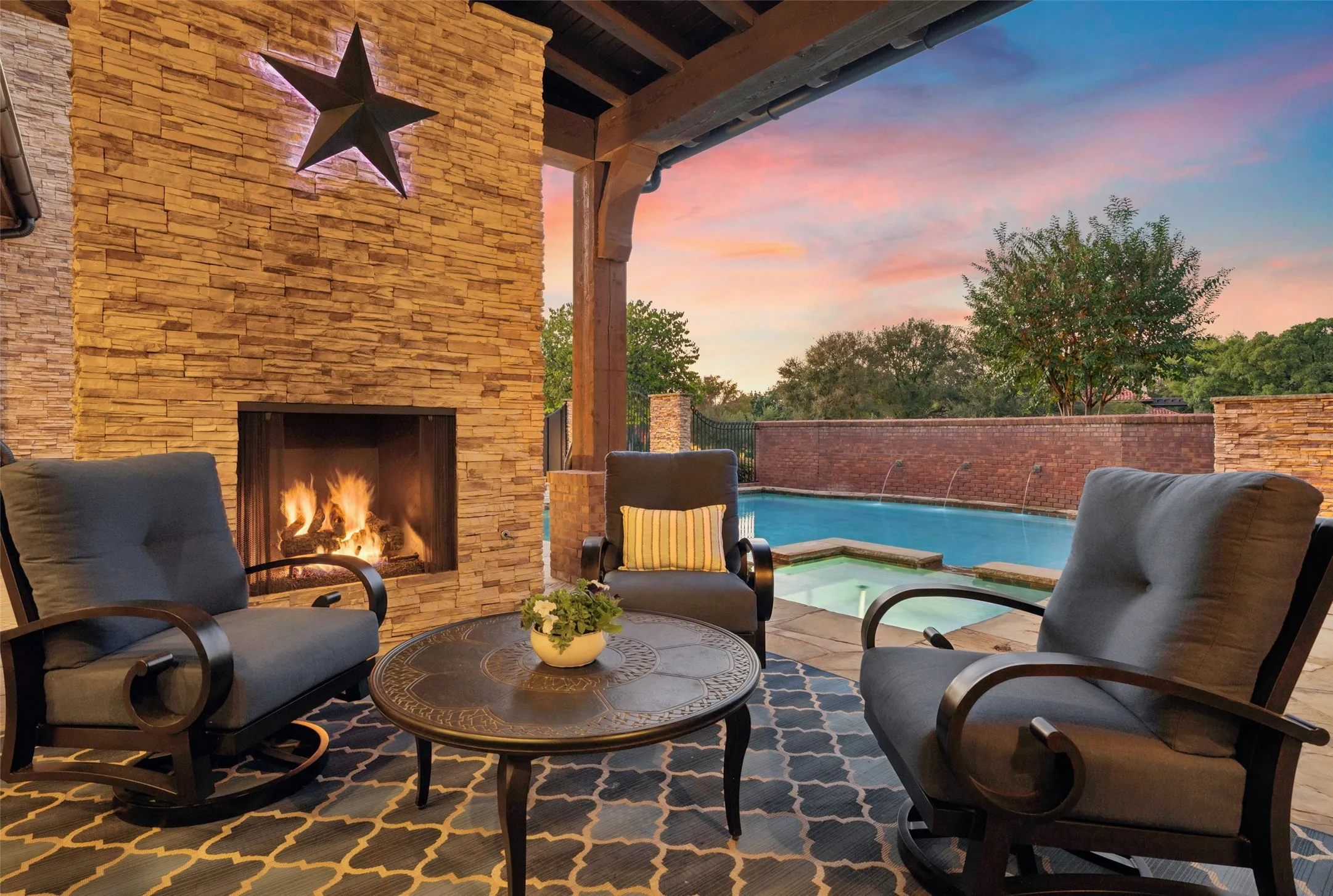 A dedicated outdoor sitting area gathers around a floor-to-ceiling stone fireplace, perfect for evening fires under the open sky.