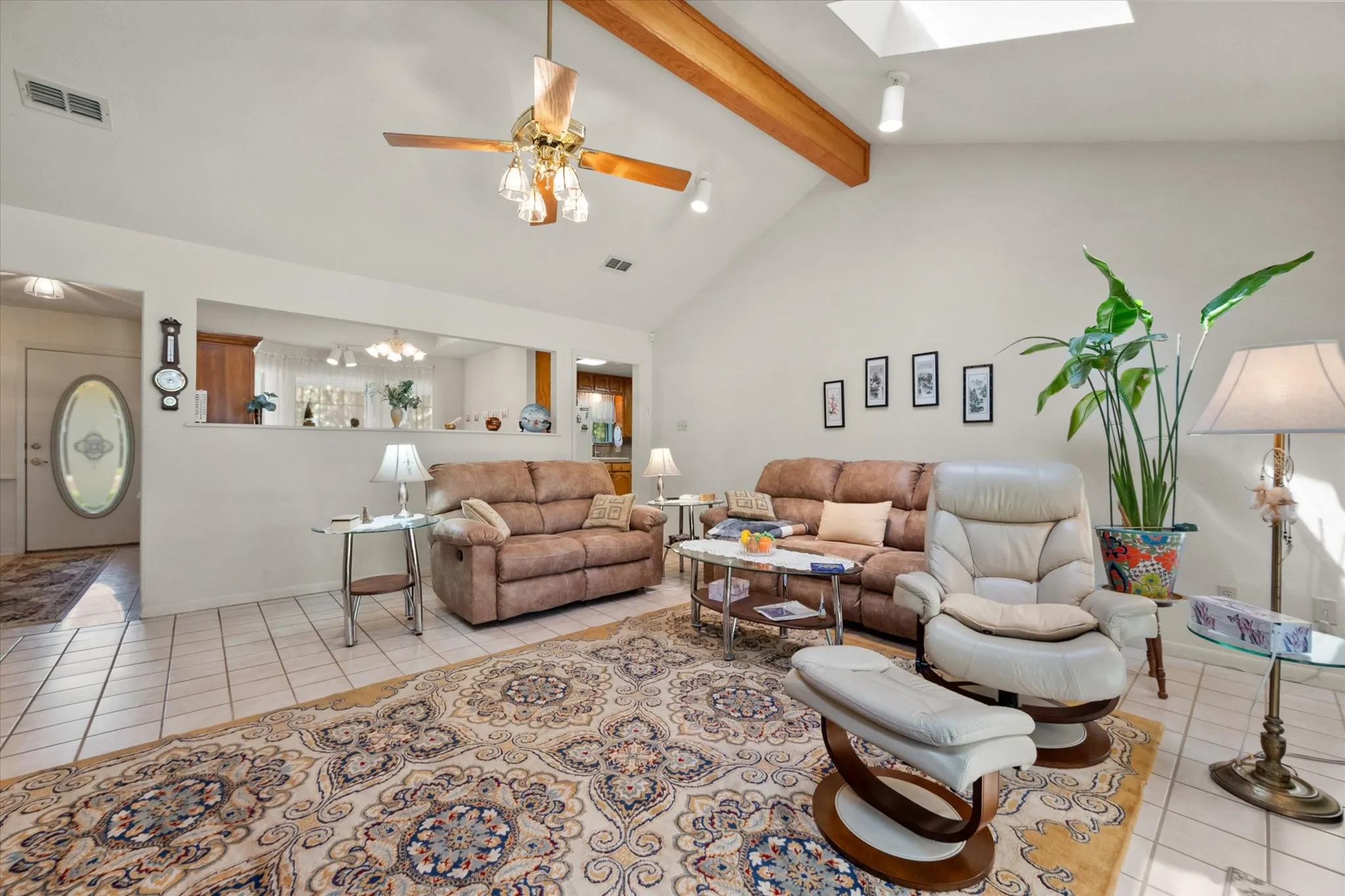 Vaulted ceiling with exposed wood beams, skylight, and ceiling fan