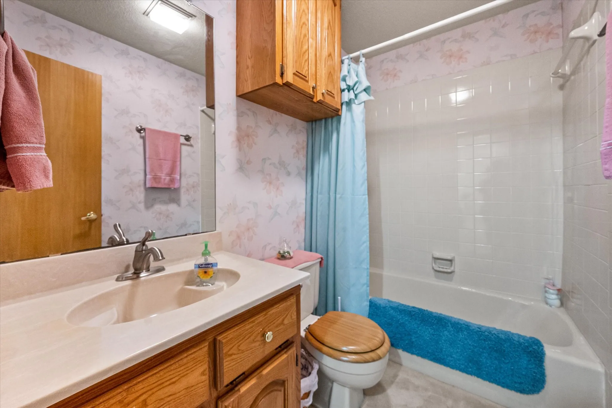 Bathroom featuring a vanity with a drop-in sink, wood-finish cabinetry, a built-in tub with tile surround, and an overhead lighting fixture