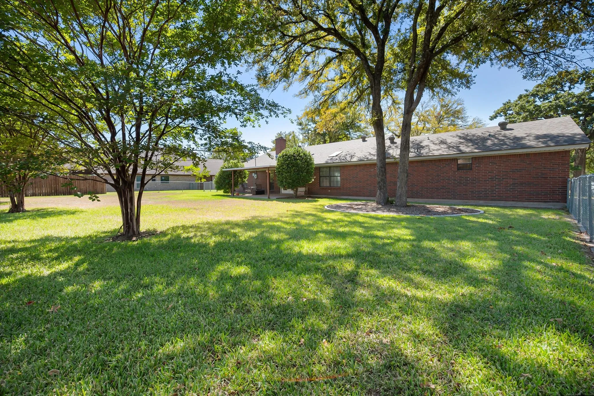 Expansive backyard featuring mature trees, a manicured lawn, and a brick exterior