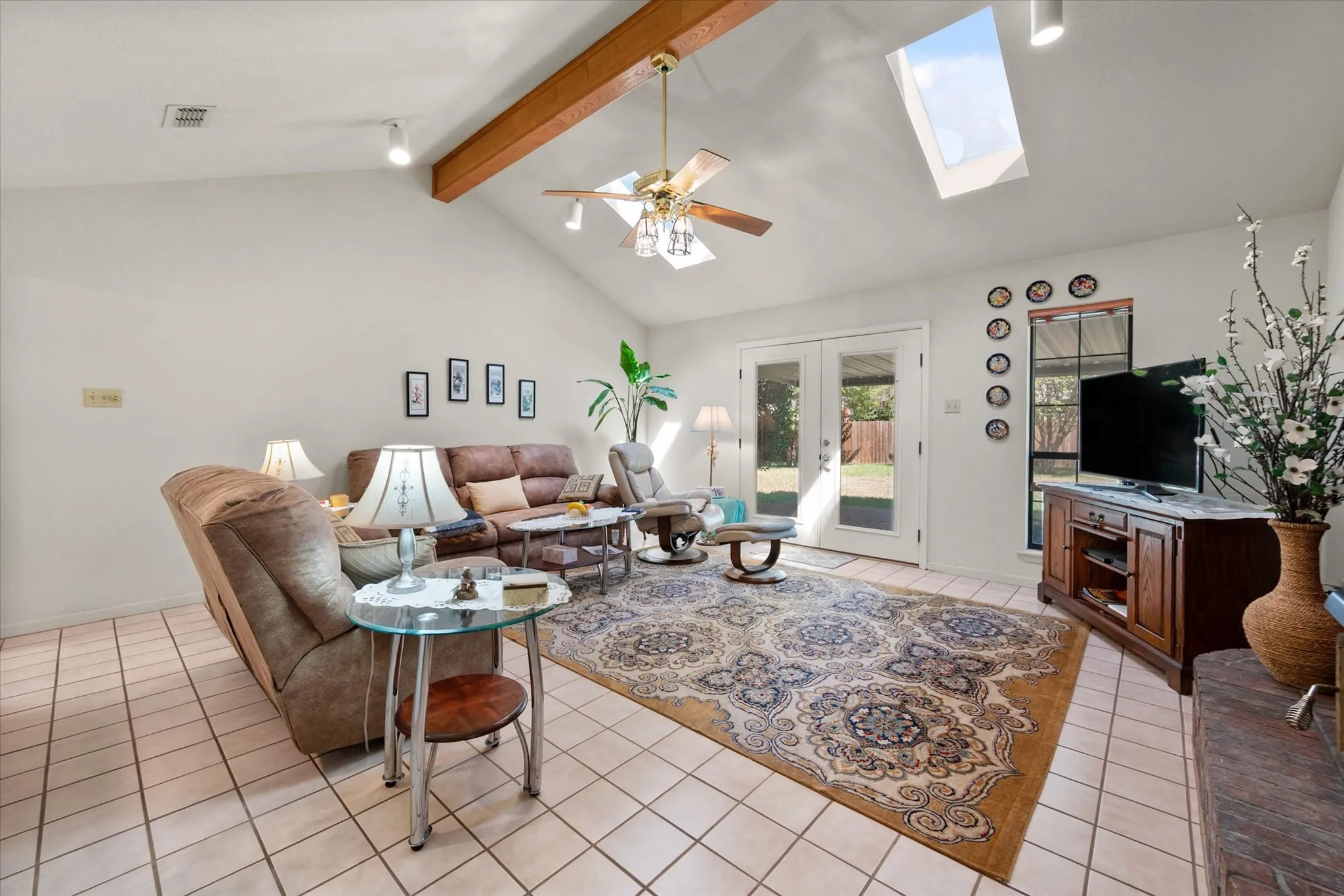 Vaulted ceiling with exposed wood beam, dual skylights, and ceramic tile flooring