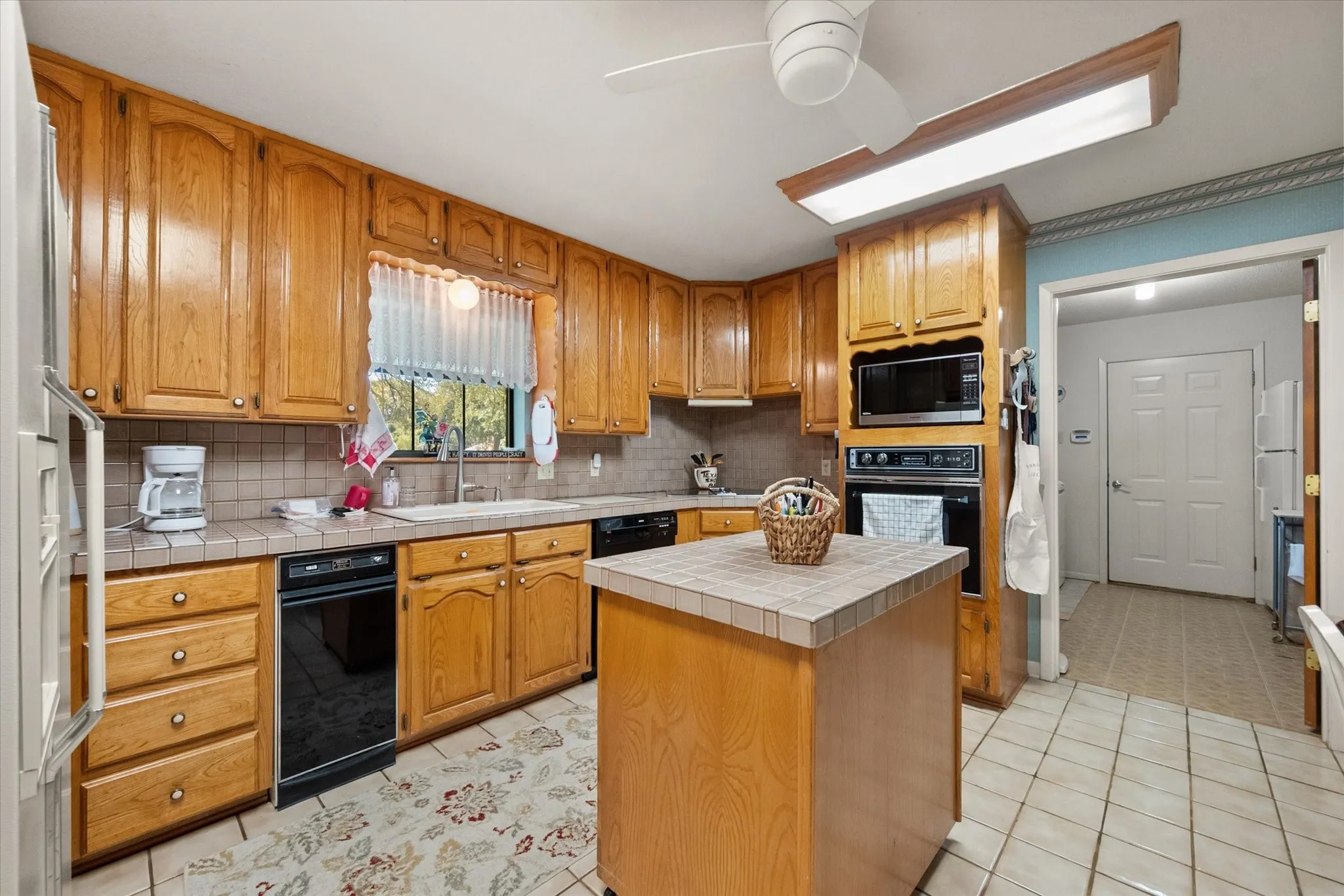 Kitchen featuring wood cabinetry, tile countertops, built-in appliances, a central island, and tile flooring