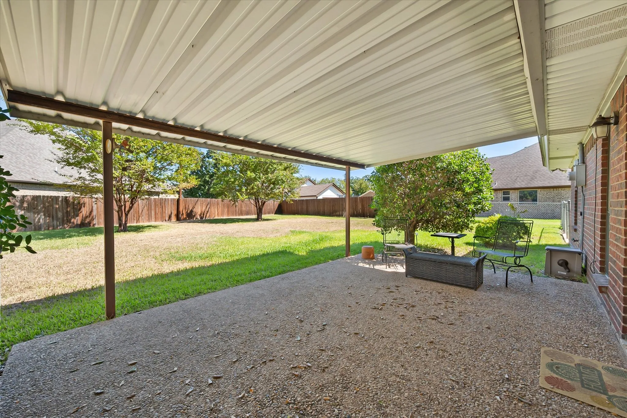Expansive backyard featuring a covered patio, brick exterior, and mature trees