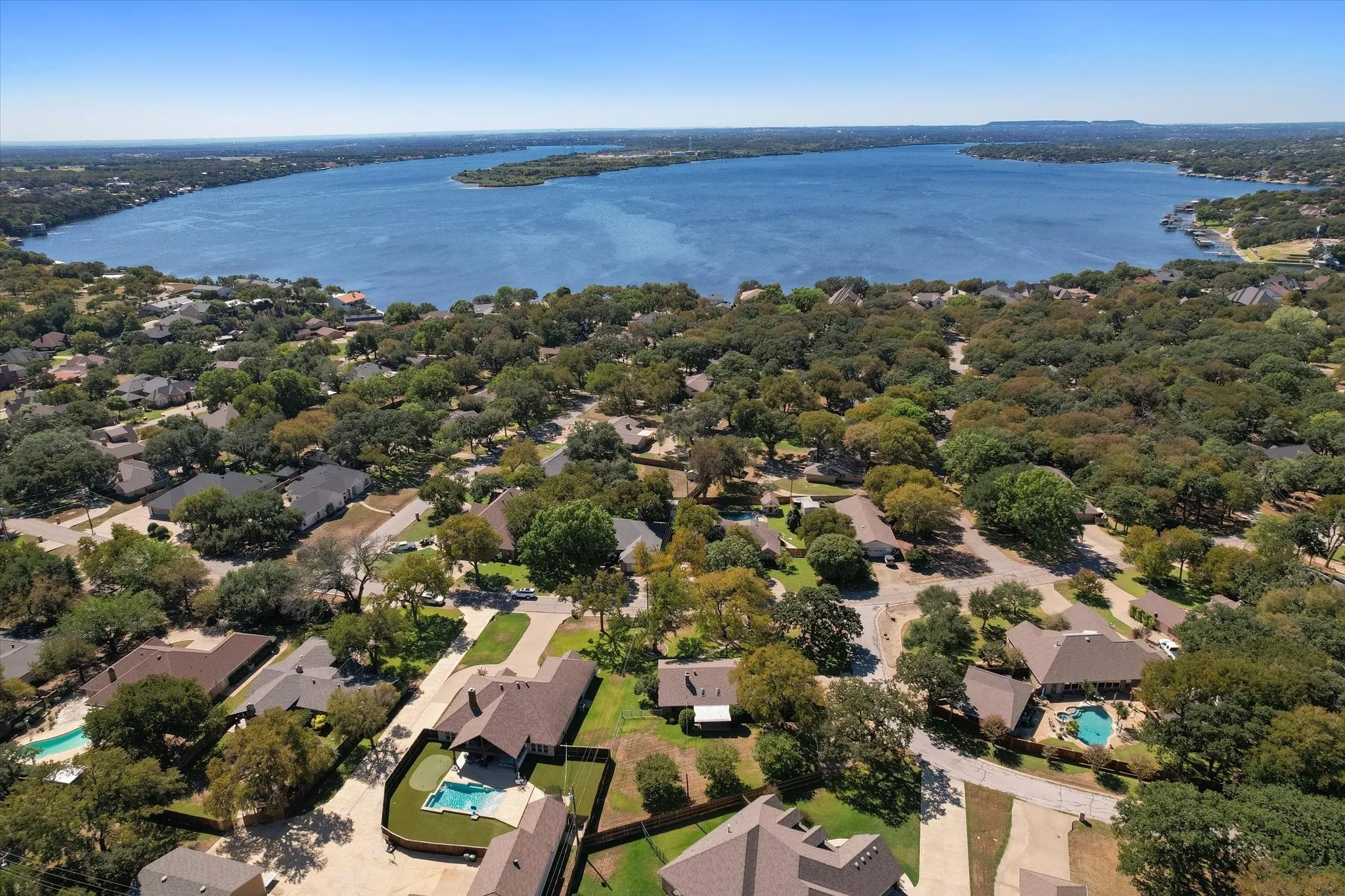Aerial perspective showcasing a residential area with a prominent body of water, featuring numerous mature trees throughout the neighborhood