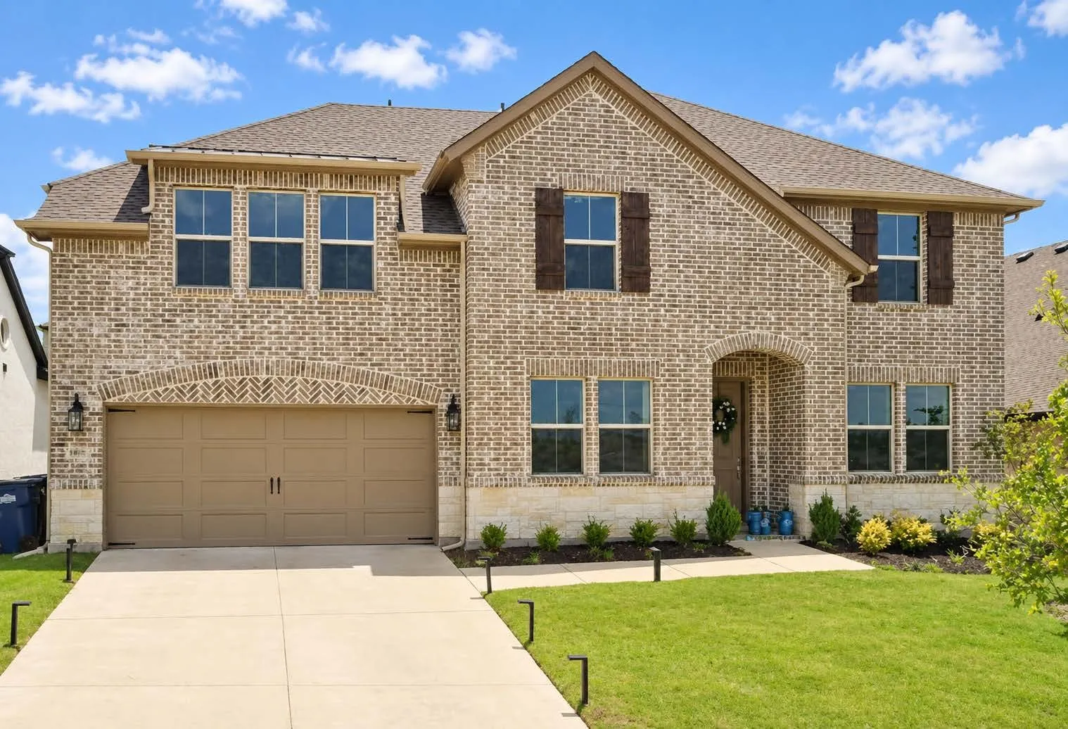 Brick exterior with stone accents, covered front entry, attached two-car garage, multiple windows, and mature landscaping