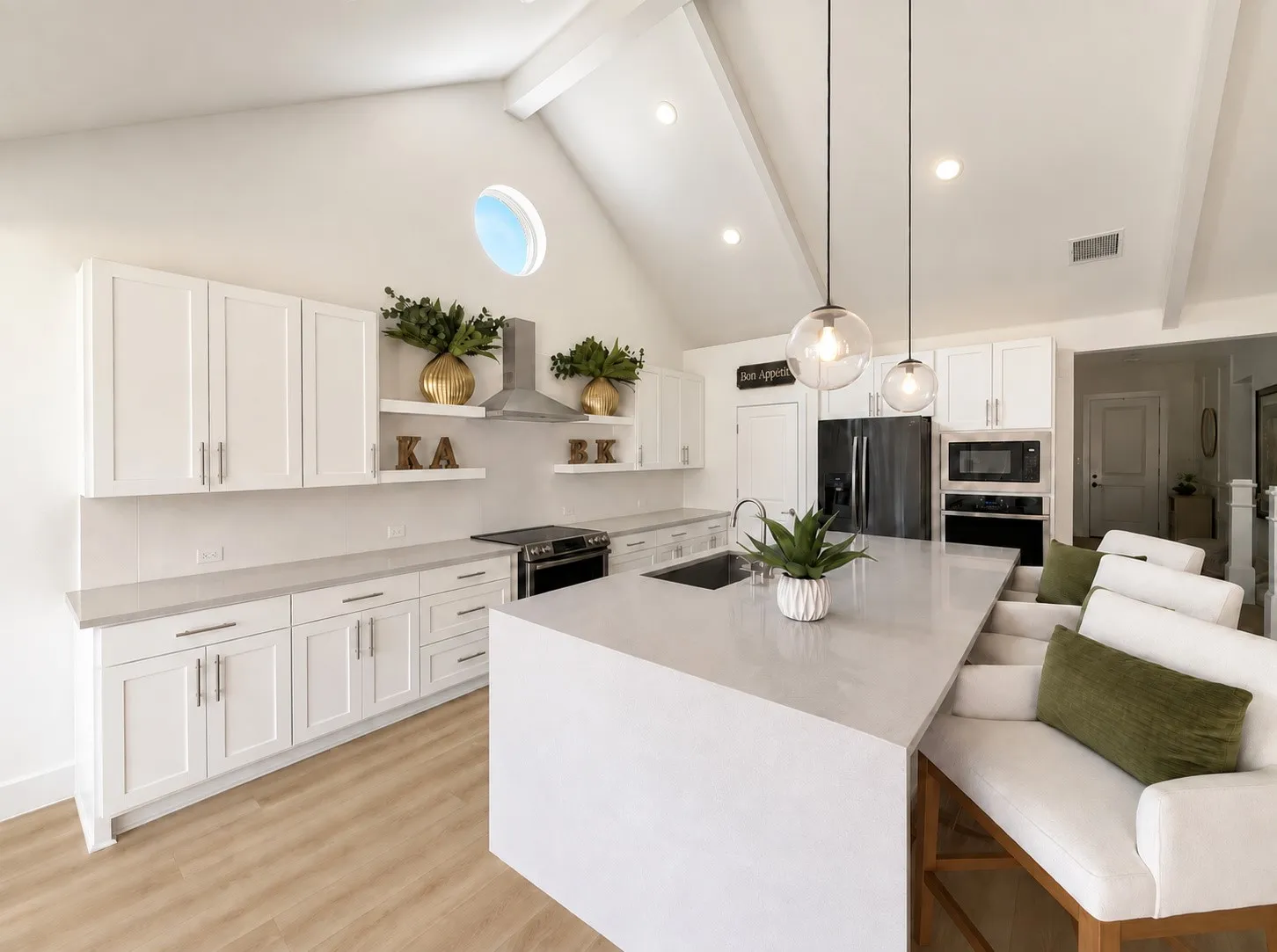 Vaulted ceiling with exposed beams, large central island with seating, pendant lighting, white shaker cabinetry, and wood-finish flooring