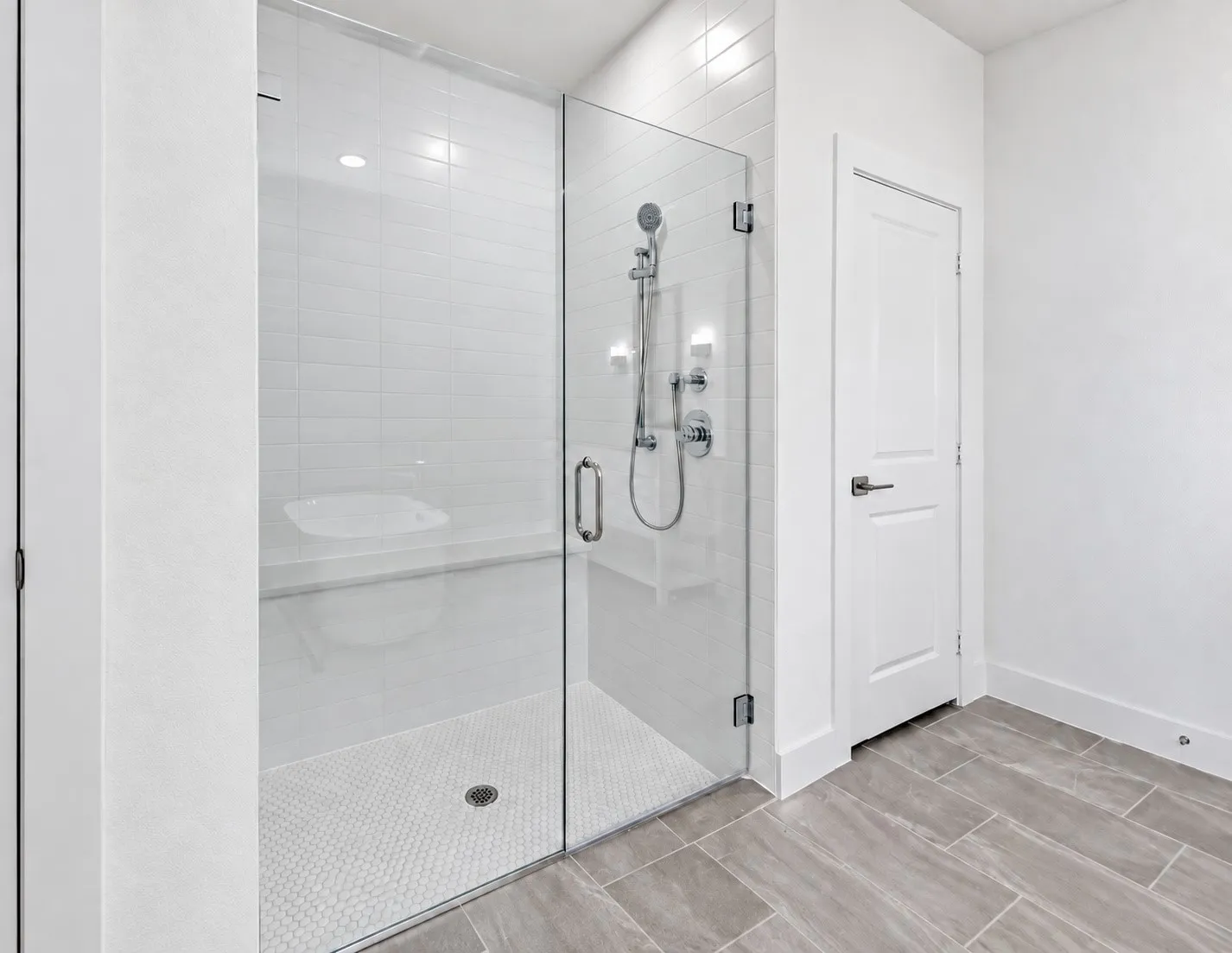 Shower with clear glass enclosure, white subway tile walls, built-in bench, and white hexagonal floor tiles
