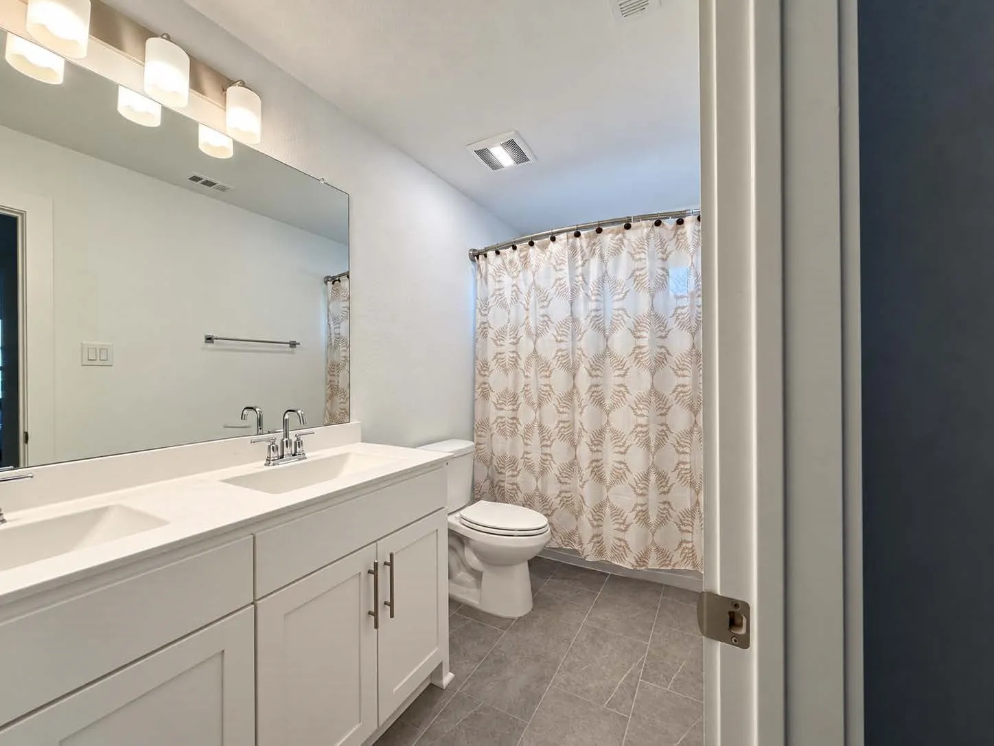 Dual basin vanity with white cabinetry, polished chrome fixtures, and a large wall-mounted mirror