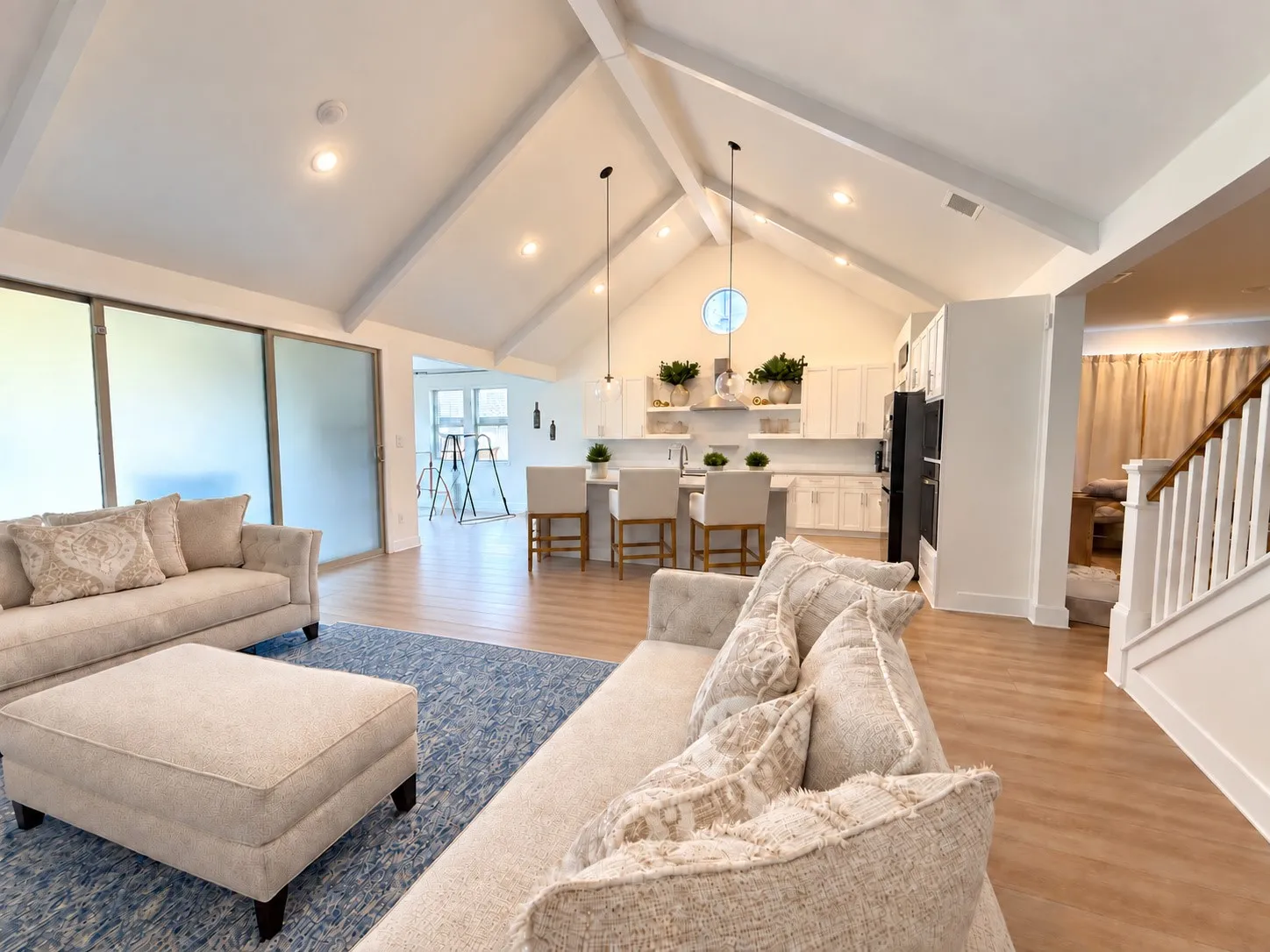 Vaulted ceilings with exposed beams, wood-finish flooring, white kitchen cabinetry, a kitchen island with seating, and a modern appliance suite