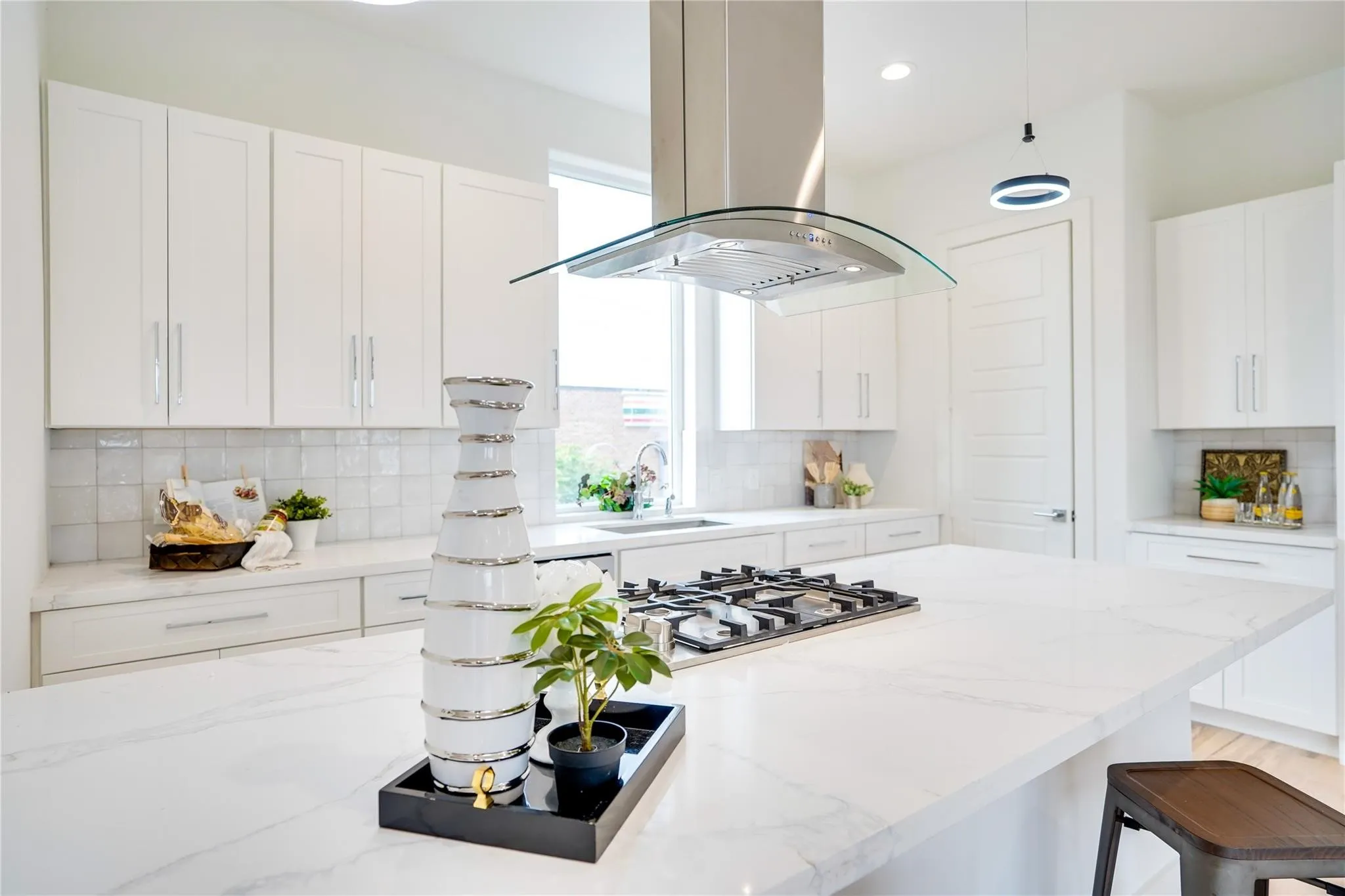 Gourmet kitchen featuring a large island with a gas cooktop, quartz countertops, white shaker cabinetry, tiled backsplash, and a modern range hood
