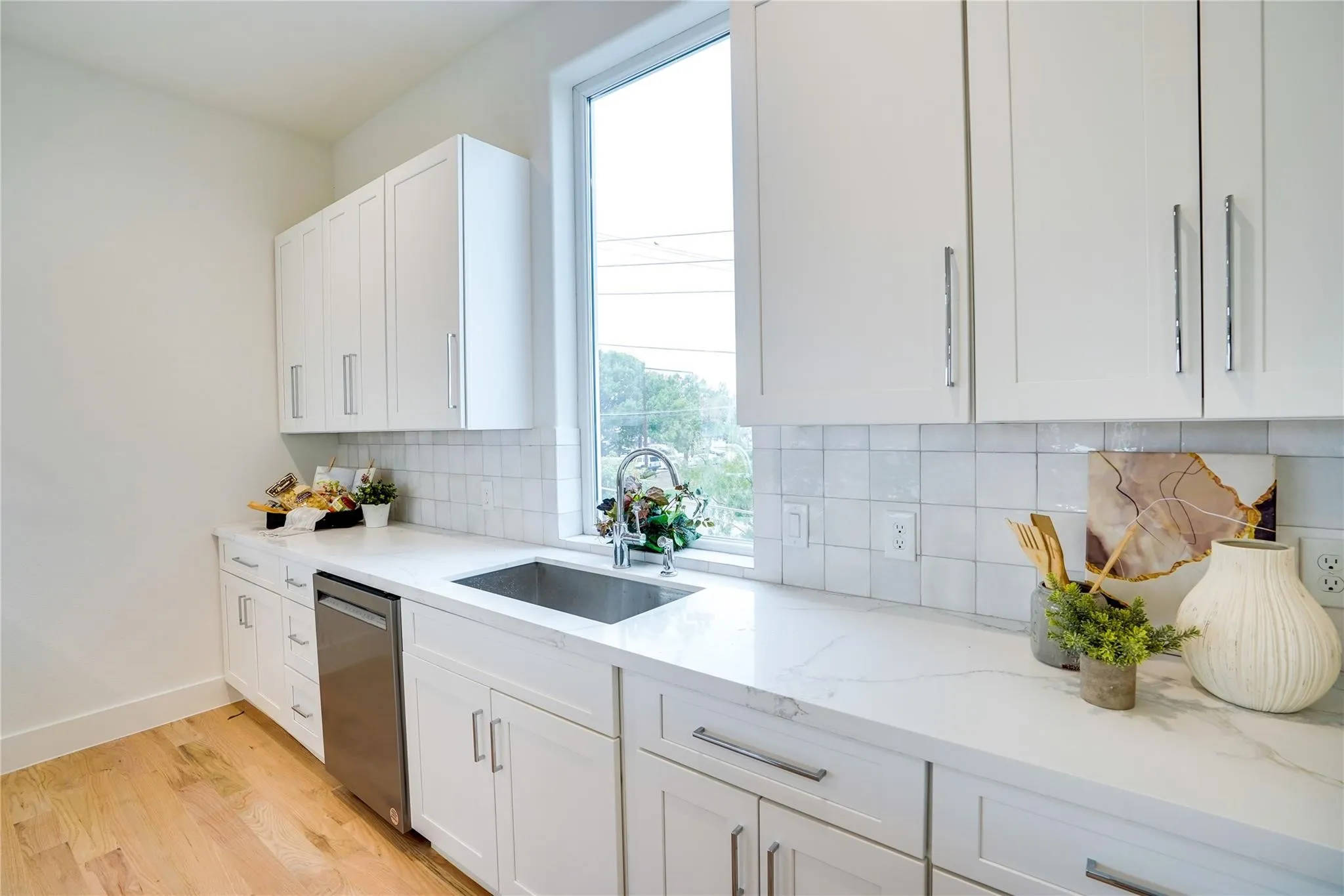 Modern kitchen featuring white cabinetry, light-toned wood-finish flooring, a stainless steel undermount sink with a gooseneck faucet, light countertops, and a subway tile backsplash