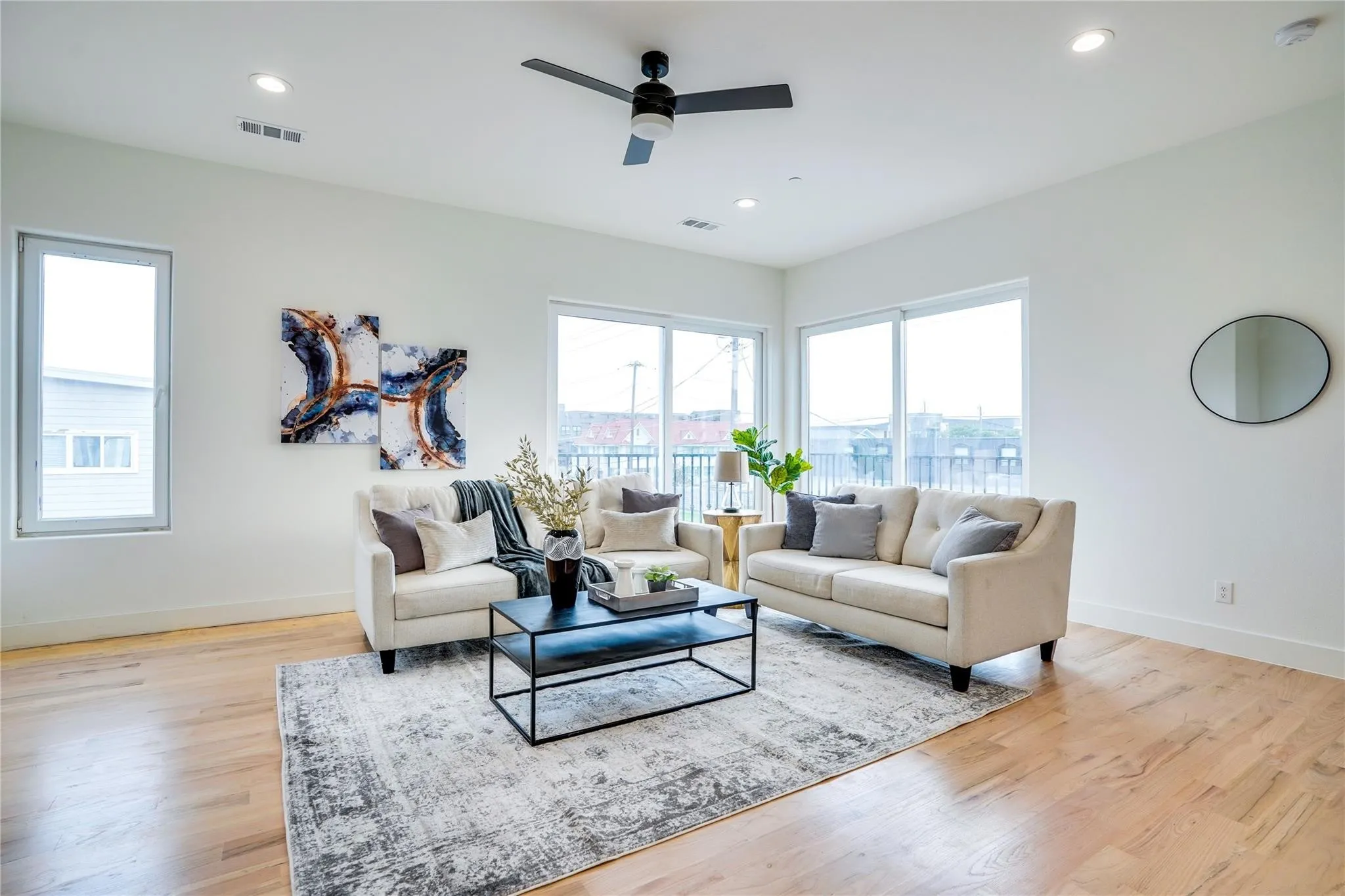 Spacious living area featuring light wood-finish flooring, white walls, and abundant natural light from multiple windows