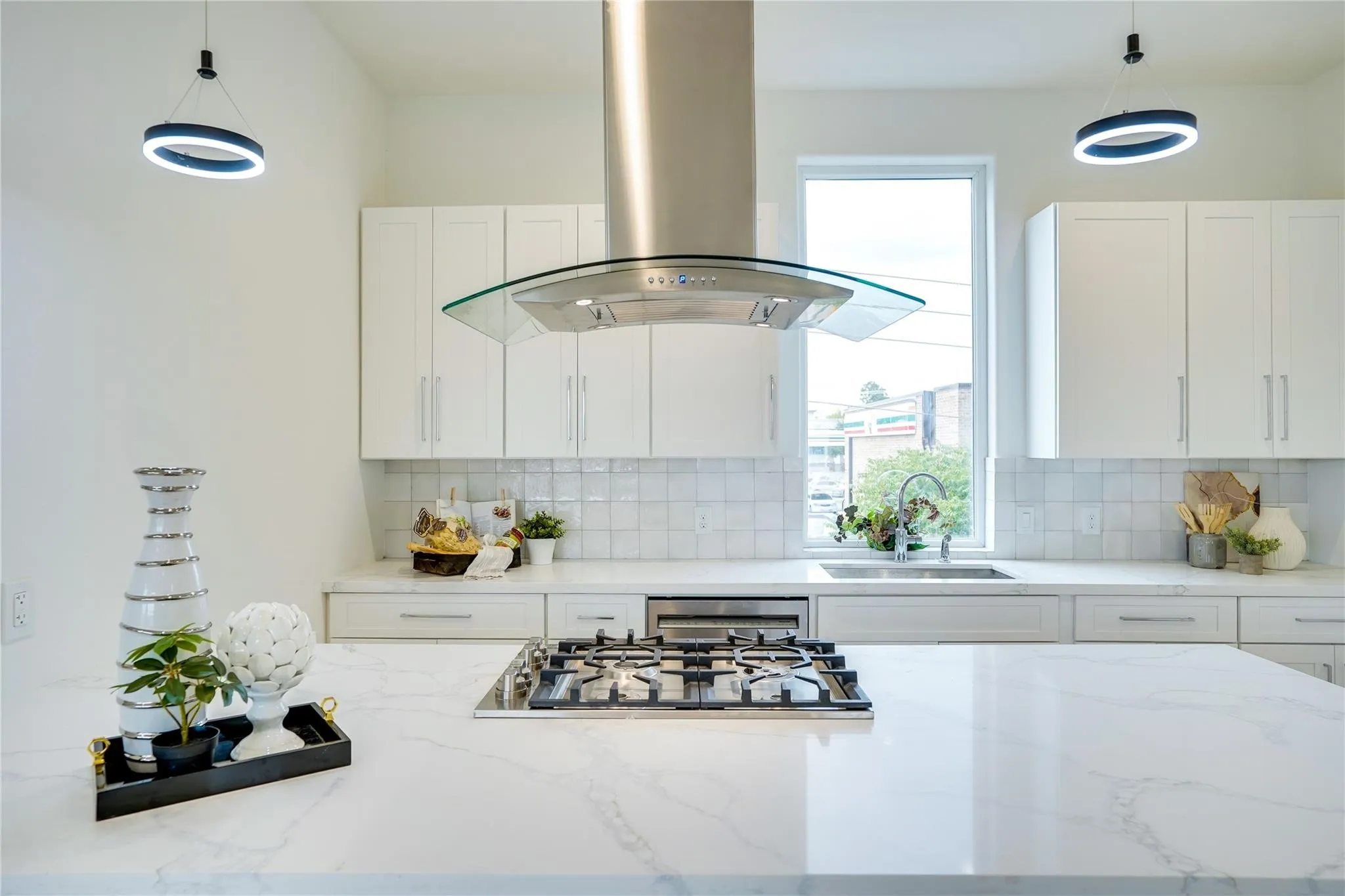 Kitchen featuring a gas range on a light-toned island, a stainless steel range hood with a glass canopy, white cabinetry, square tiled backsplash, and recessed sink under a large window