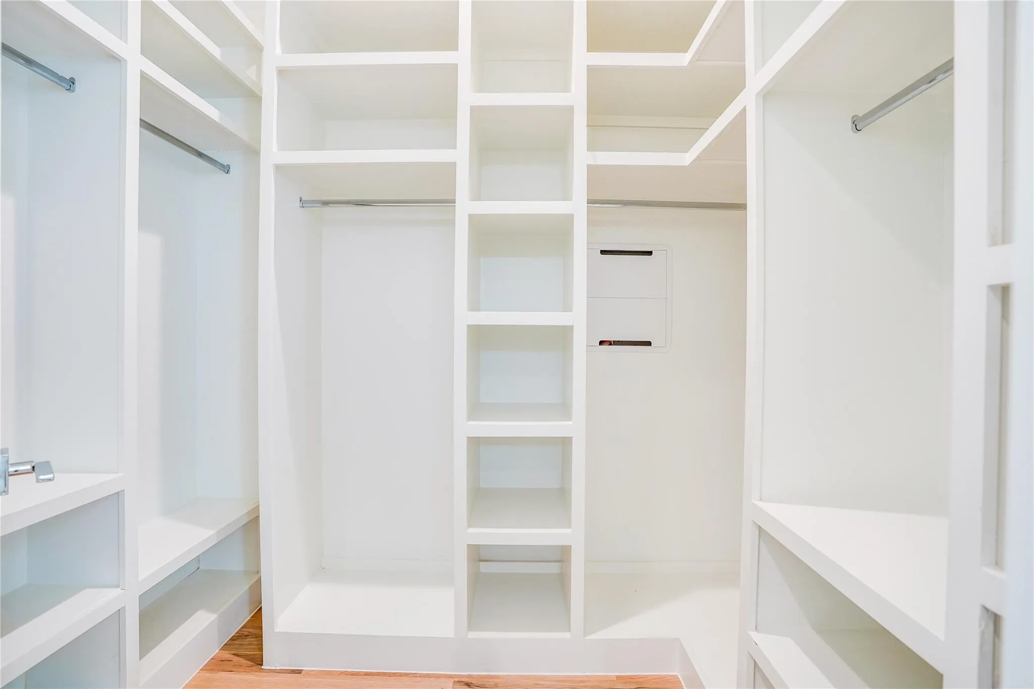 Walk-in closet featuring built-in white shelving, multiple hanging rods, and wood-finish flooring