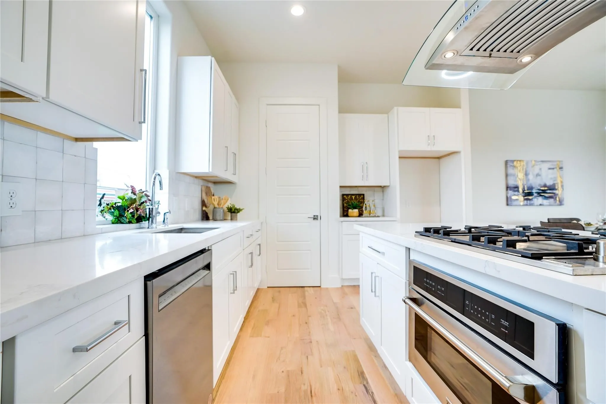 Modern kitchen featuring white cabinetry, light countertops, wood-finish flooring, a stainless steel dishwasher, and a built-in oven with a gas cooktop