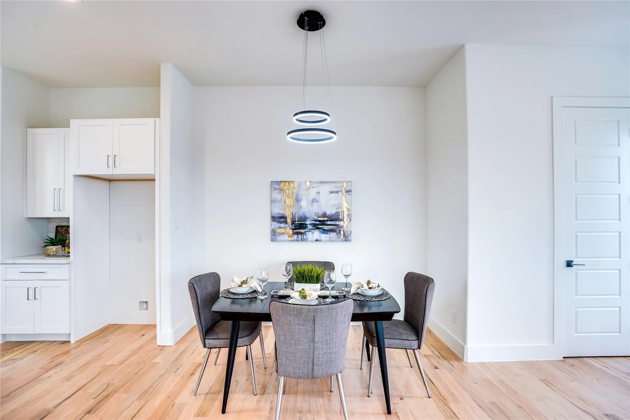 Bright dining area featuring wood-finish flooring, a modern chandelier, and a five-panel interior door with matte black hardware