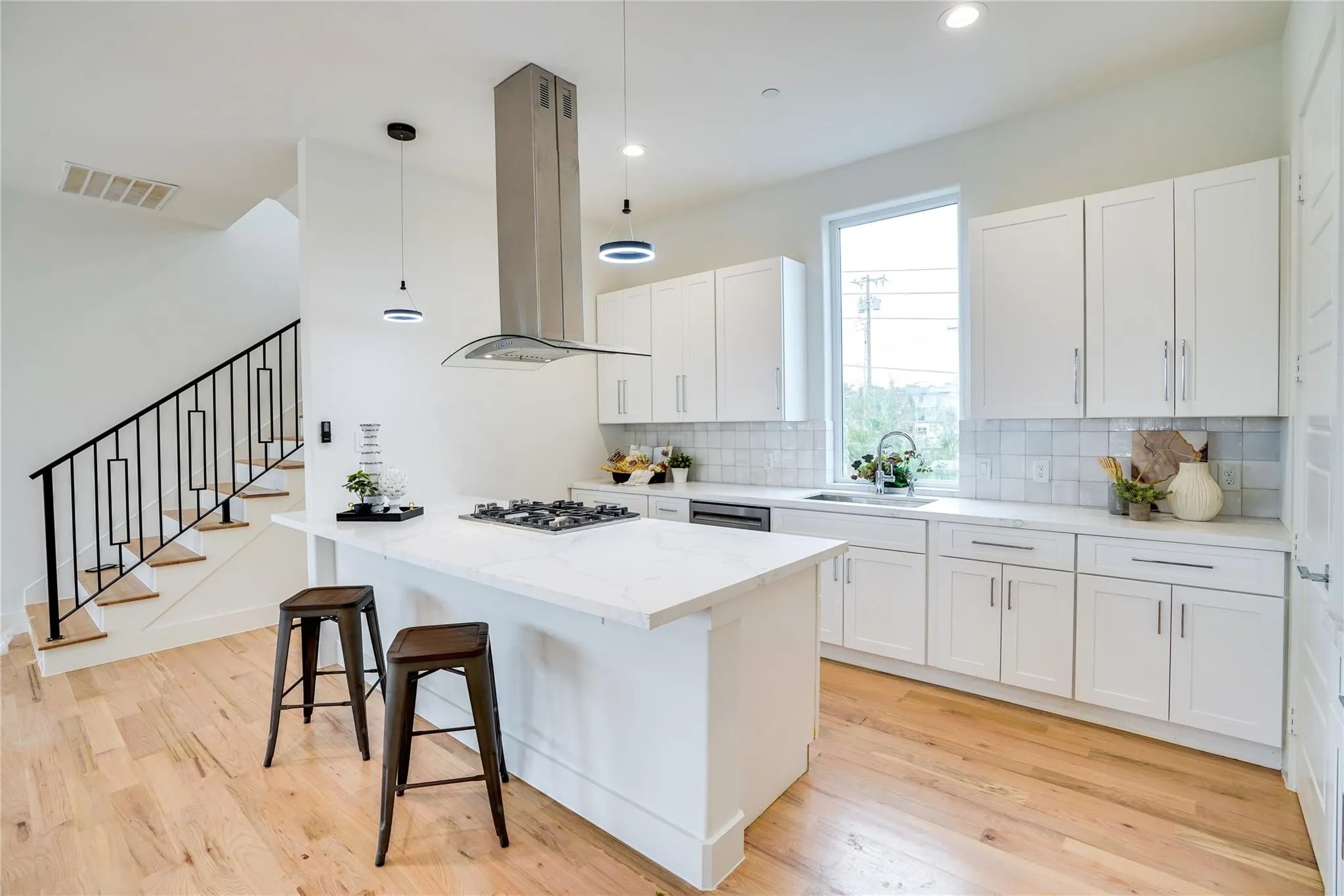 Contemporary kitchen featuring a center island with a built-in gas cooktop, white cabinetry, light-toned wood-finish flooring, a stainless steel range hood, and a full-height window