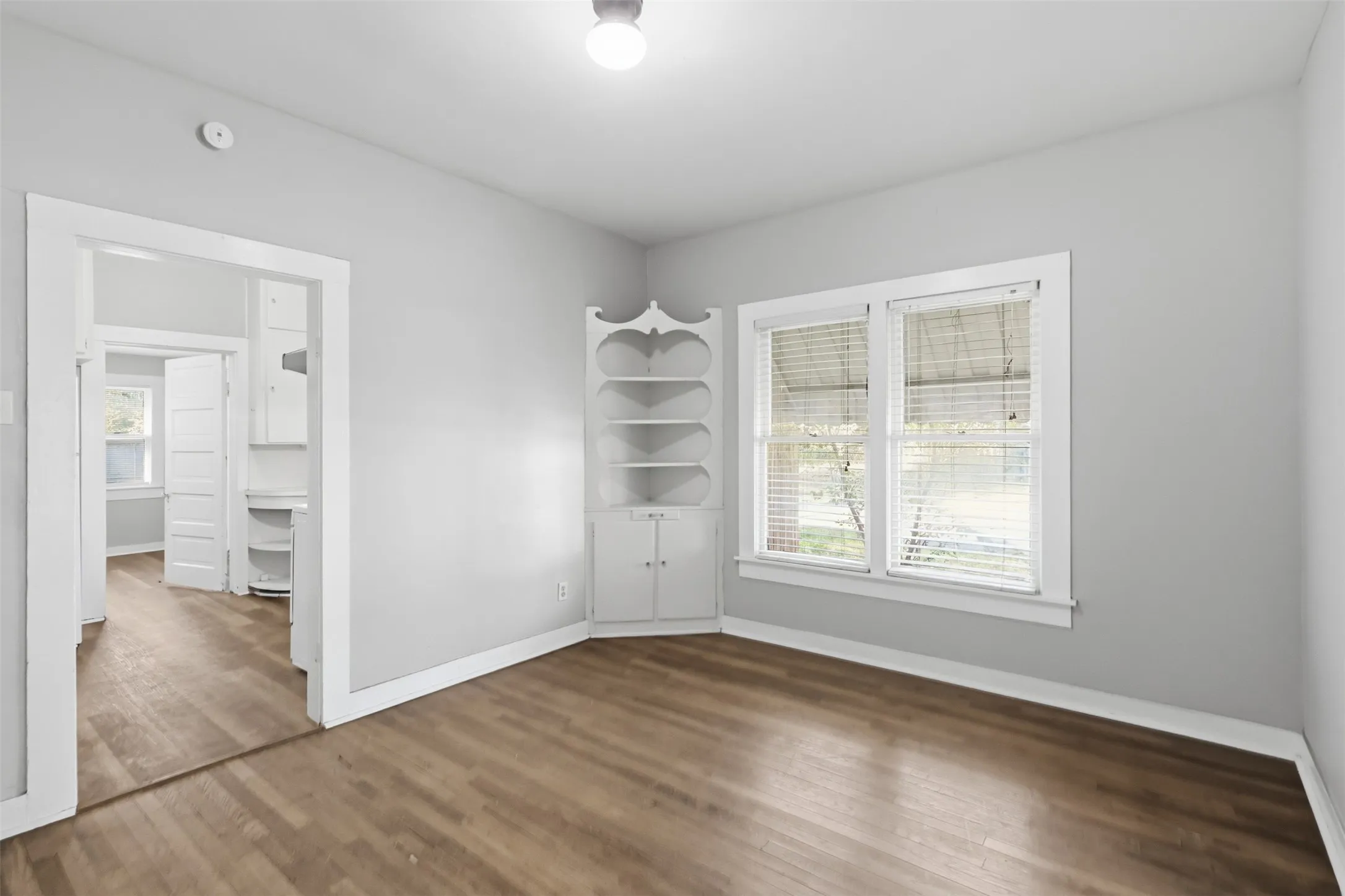 Wood-finish flooring, white built-in corner shelving, white window trim, and overhead lighting