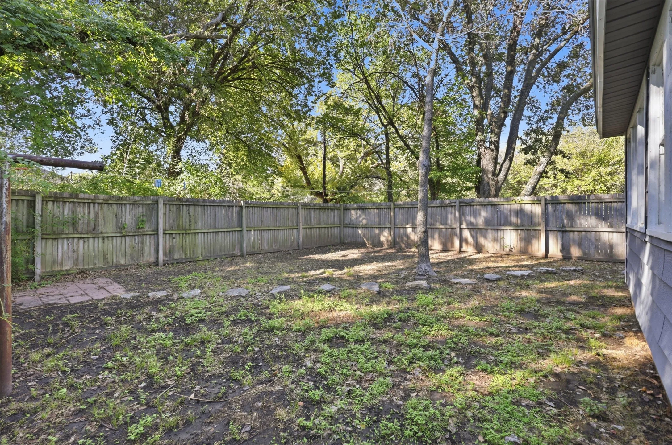 Fenced backyard with mature trees and stepping stones