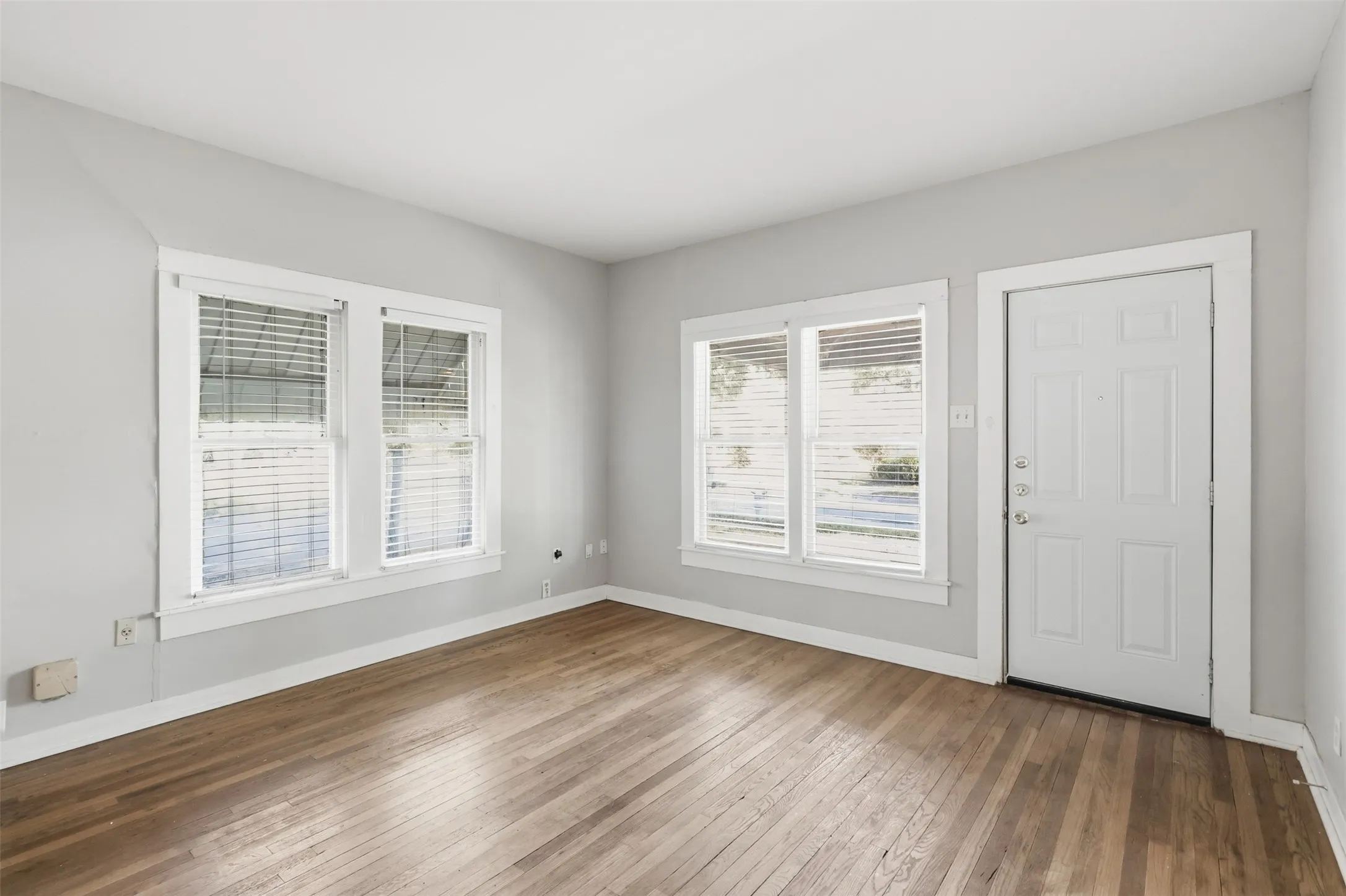 Hardwood flooring, light gray wall paint, white trim, multiple windows, and a paneled entry door