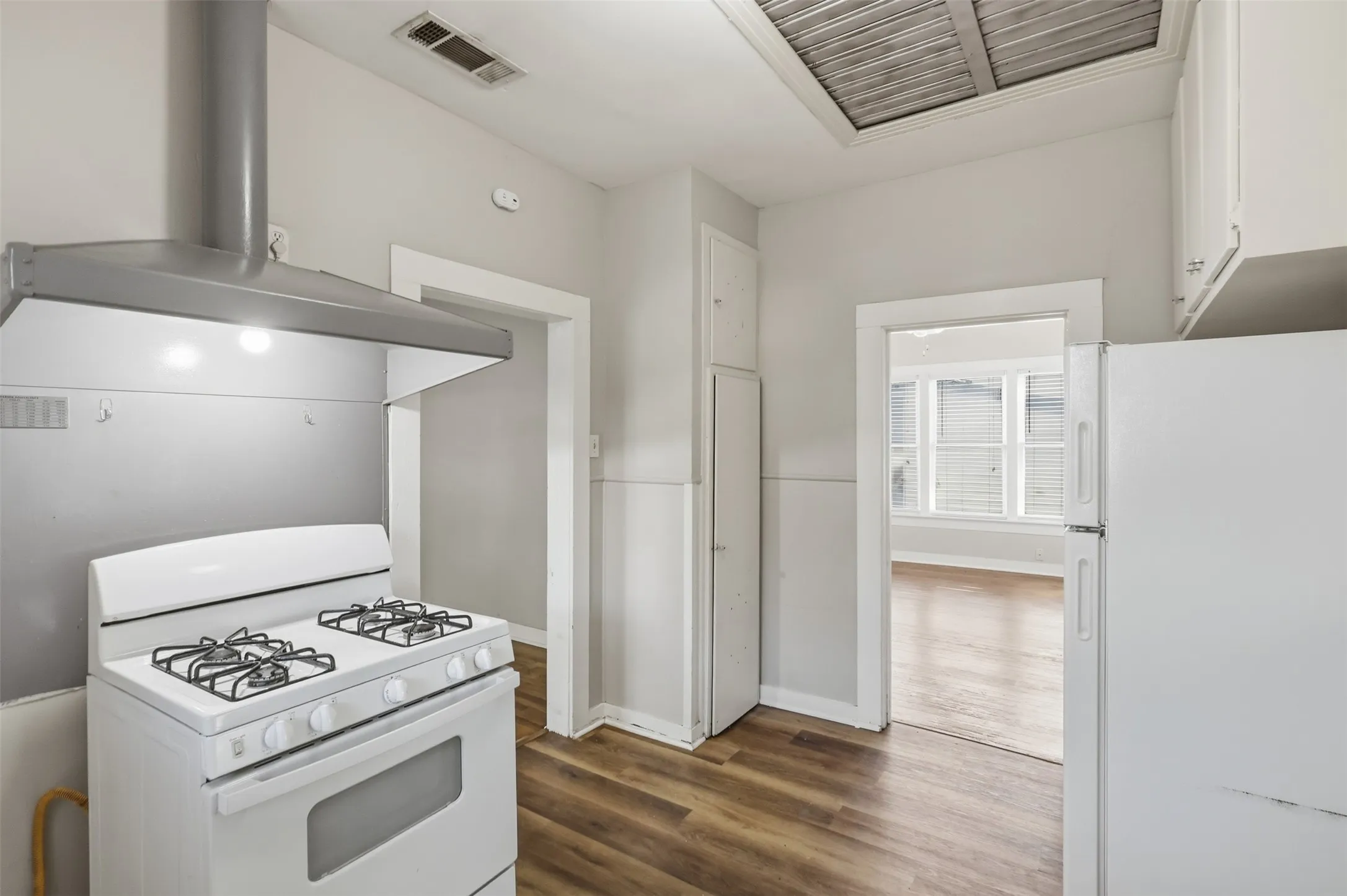Kitchen featuring wood-finish flooring, white cabinetry, a freestanding gas range, and a stainless steel range hood