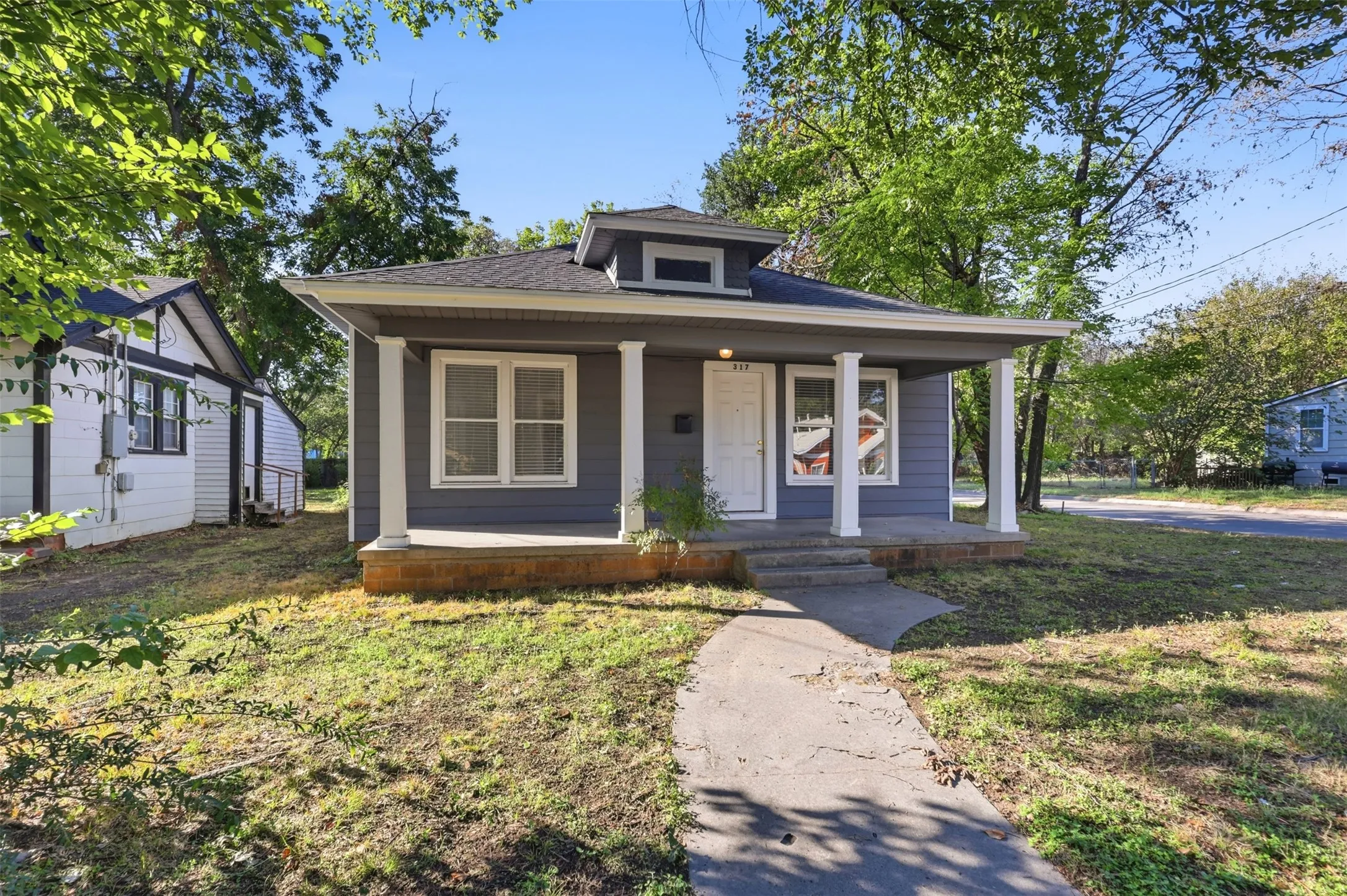 Single-story home featuring a covered front porch with white columns, light gray siding, and a contrasting dark roof
