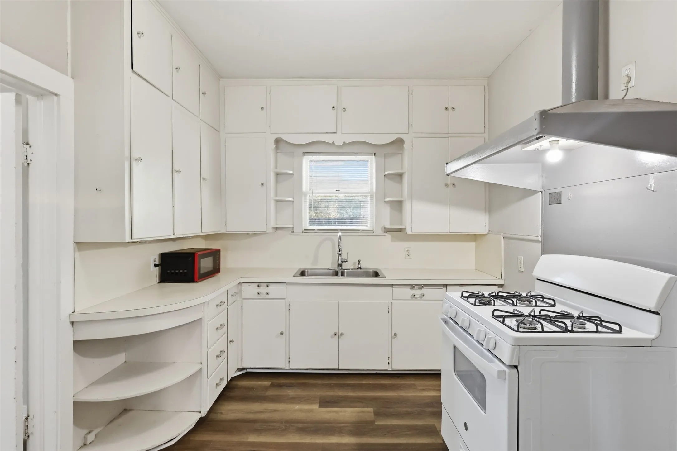 White cabinetry, wood-finish flooring, built-in shelving, dual basin sink, and a gas range
