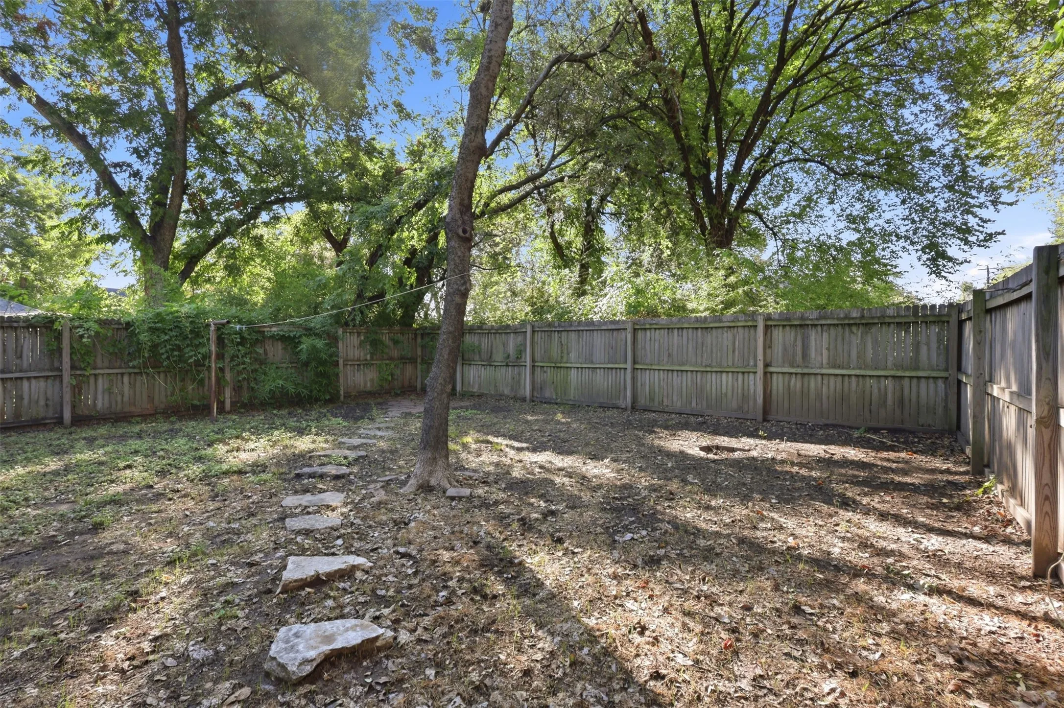 Fenced backyard featuring mature trees and a stone pathway