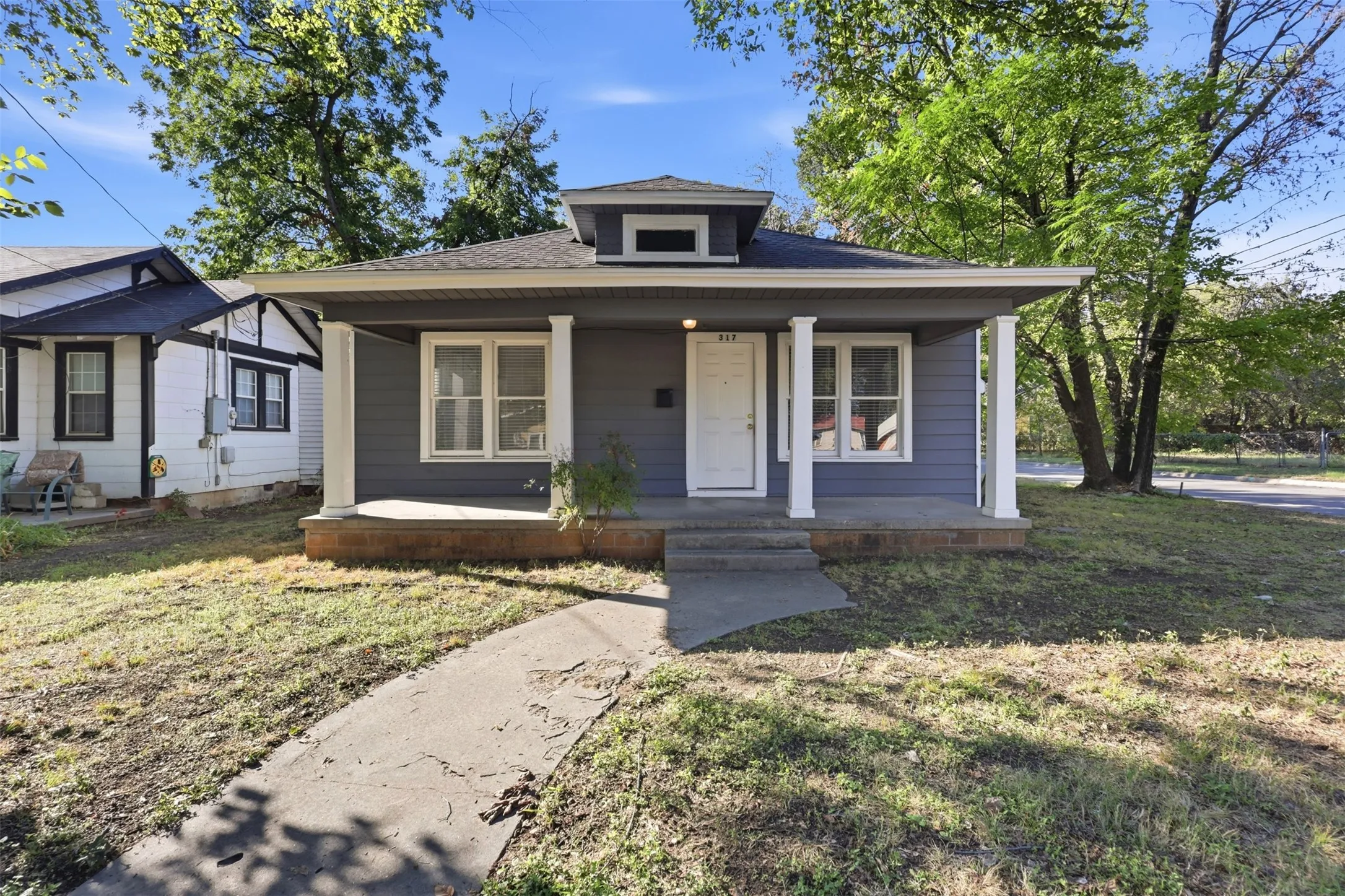 Blue siding with white trim, covered front porch, white columns, concrete walkway, and a dormer window