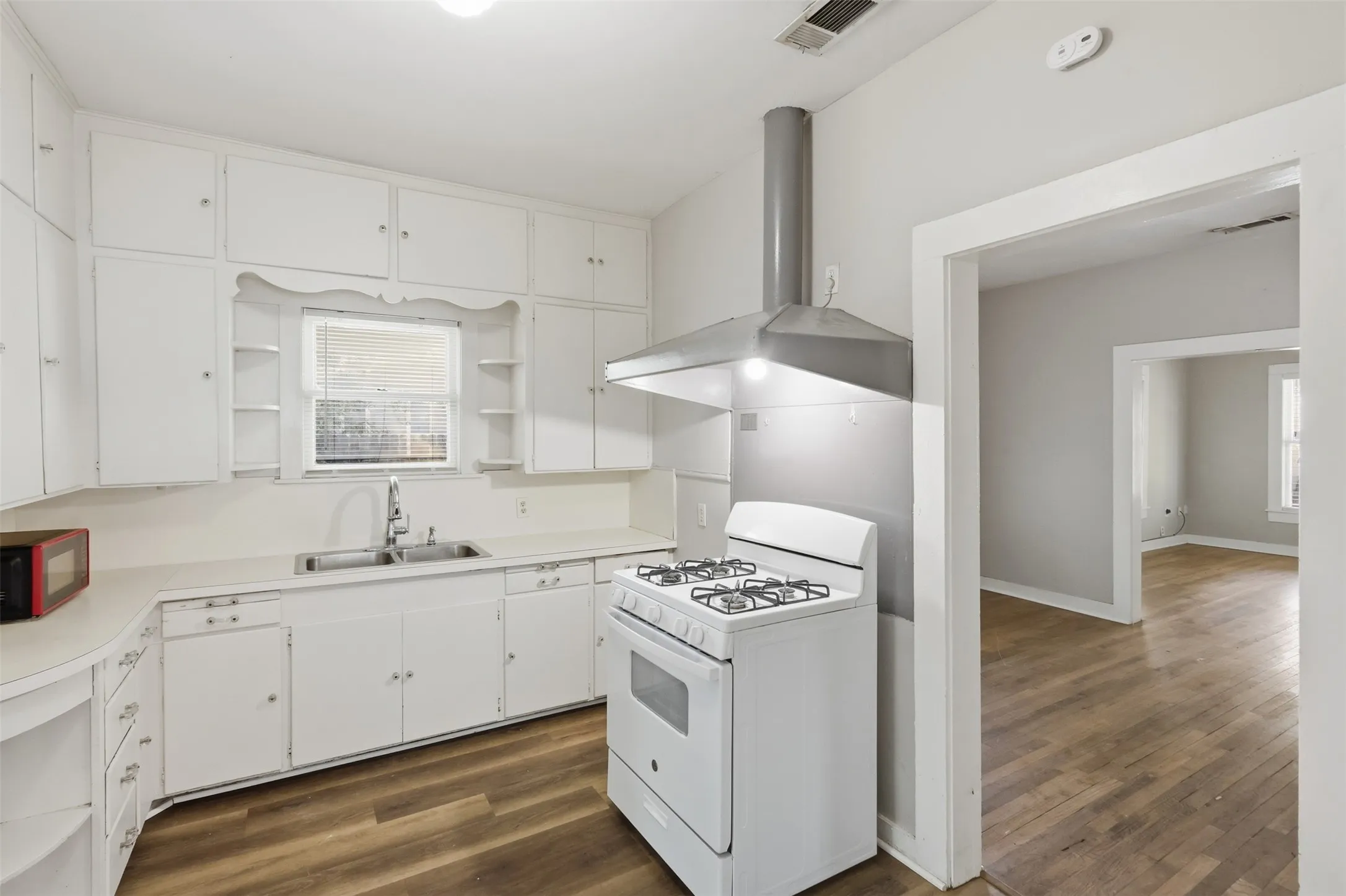White cabinetry, dual basin sink with chrome faucet, gas range, stainless steel range hood, wood-finish flooring