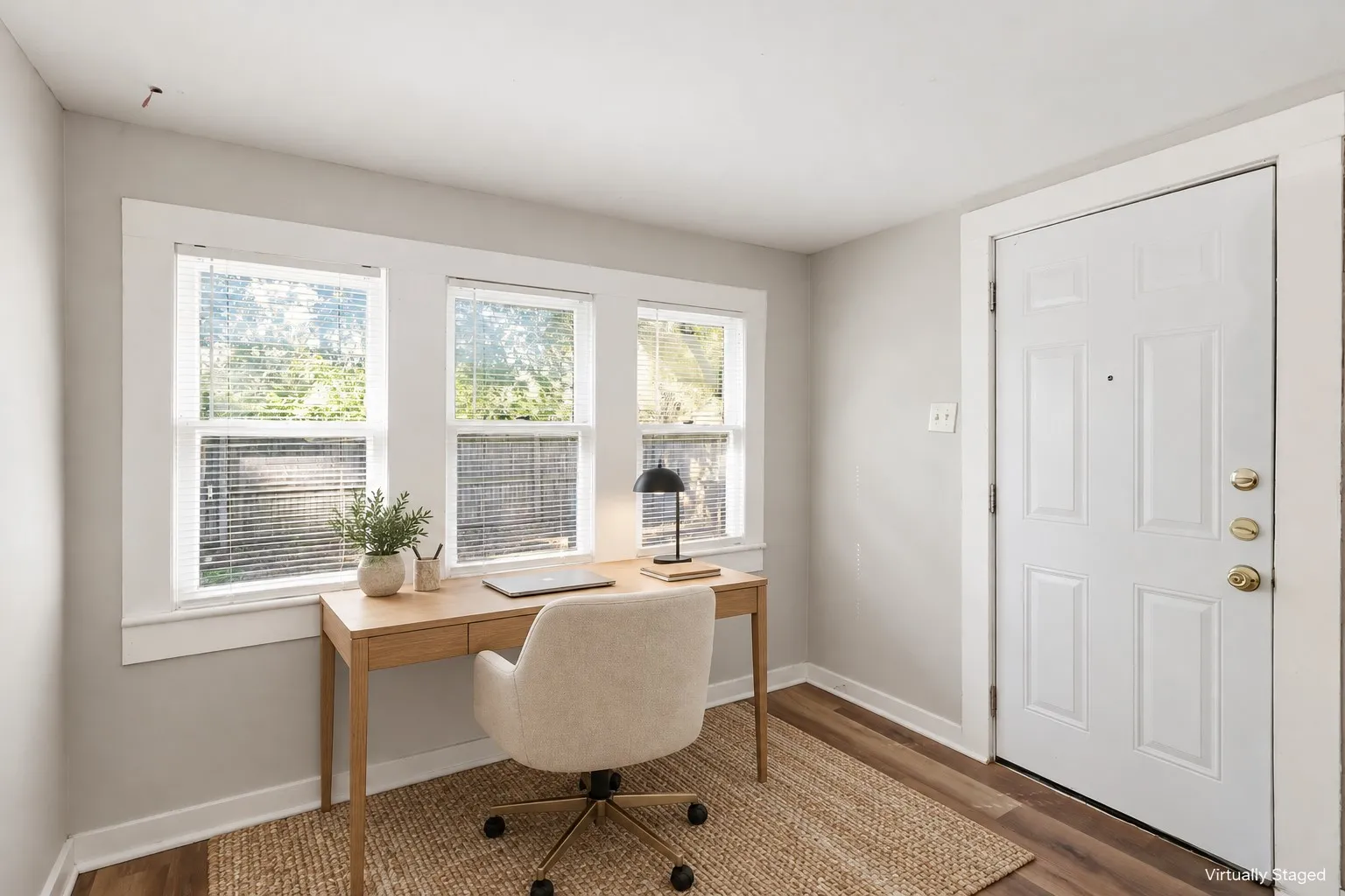 Wood-finish flooring with a light gray wall color, white trim, and a white paneled door with brass hardware