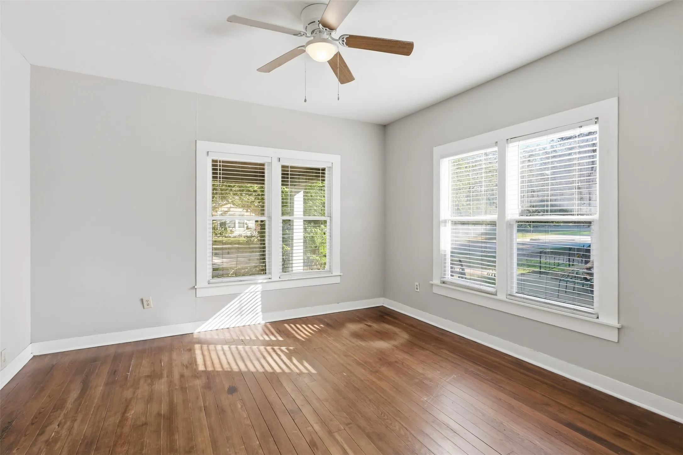 Hardwood flooring, painted walls, two windows with blinds, and a ceiling fan with integrated lighting
