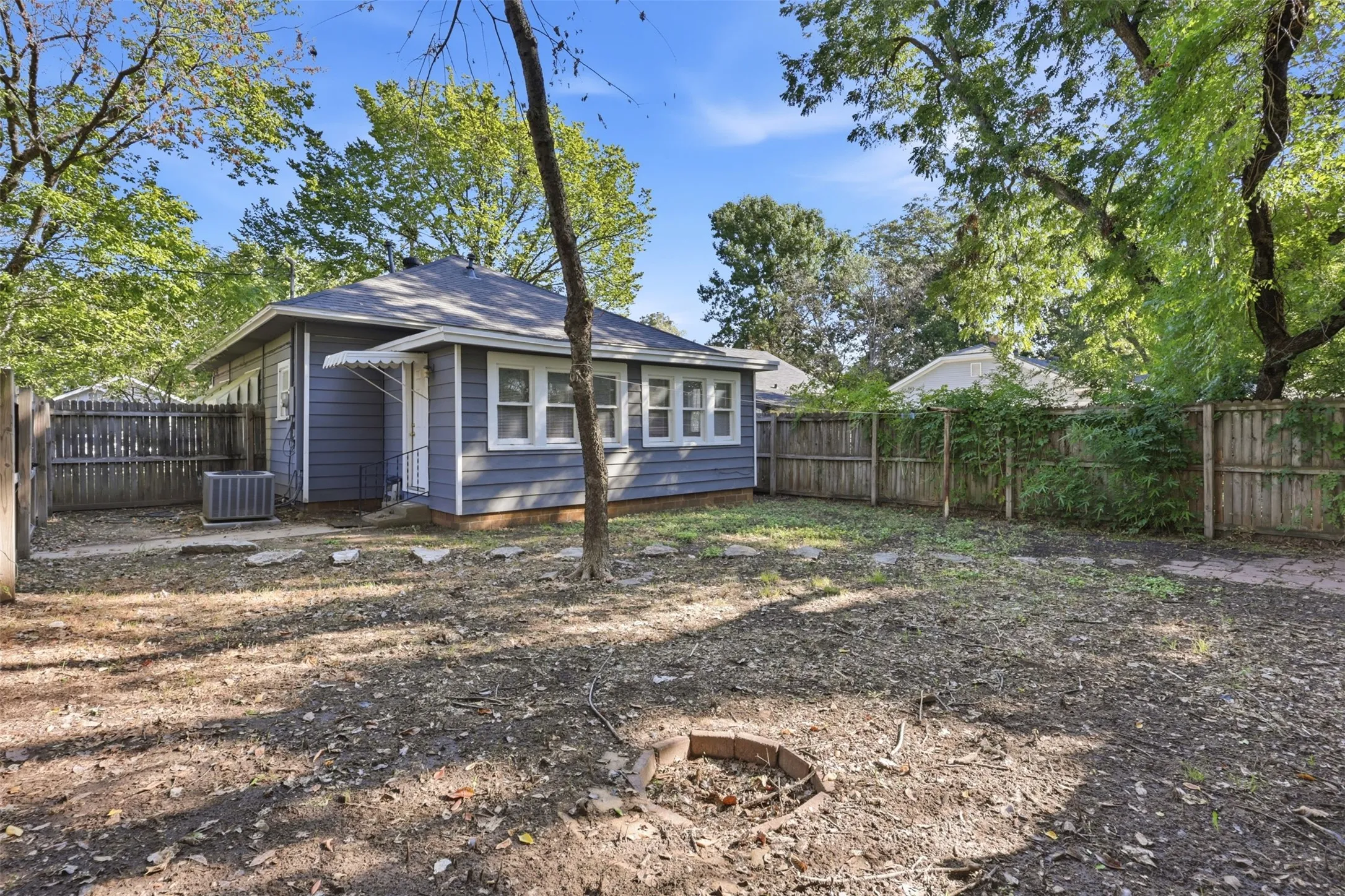 Rear exterior featuring blue siding, white trim windows, an air conditioning unit, and a fenced perimeter