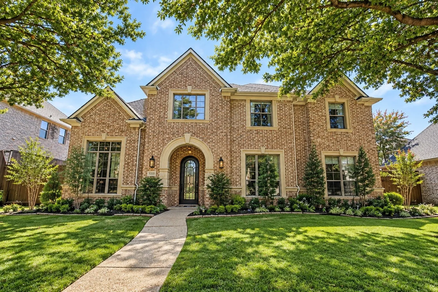 Brick exterior with decorative stone accents, arched entry, formal landscaping, and a manicured lawn