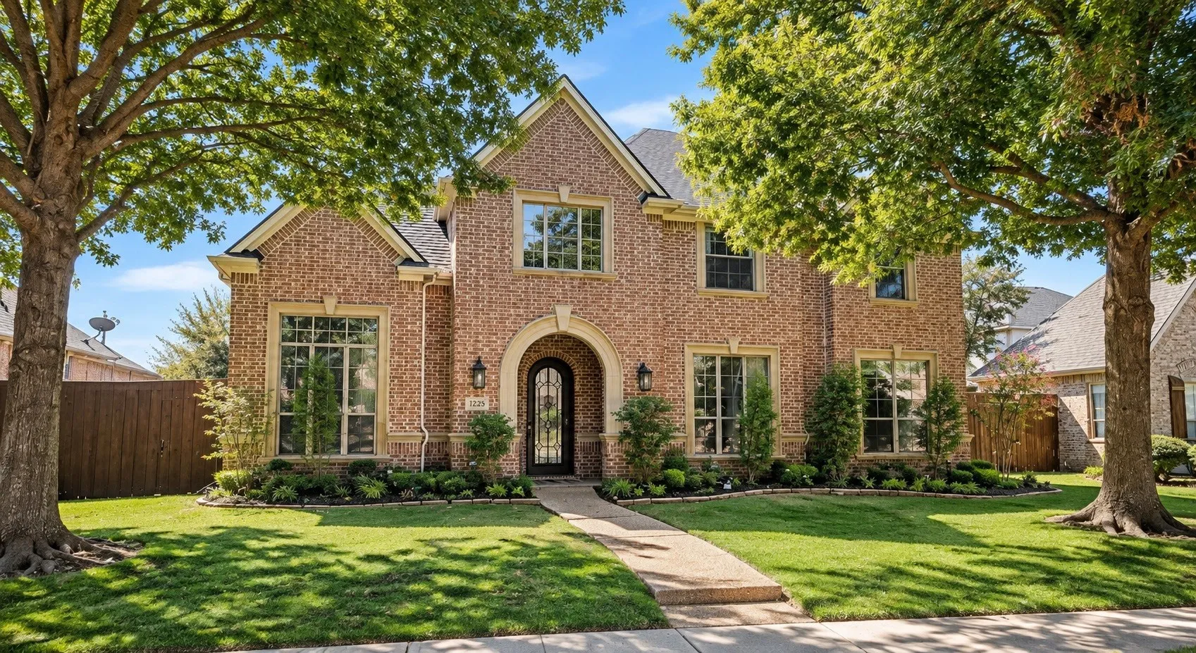 Brick exterior with stone accents, arched entry, mature landscaping, and a manicured lawn