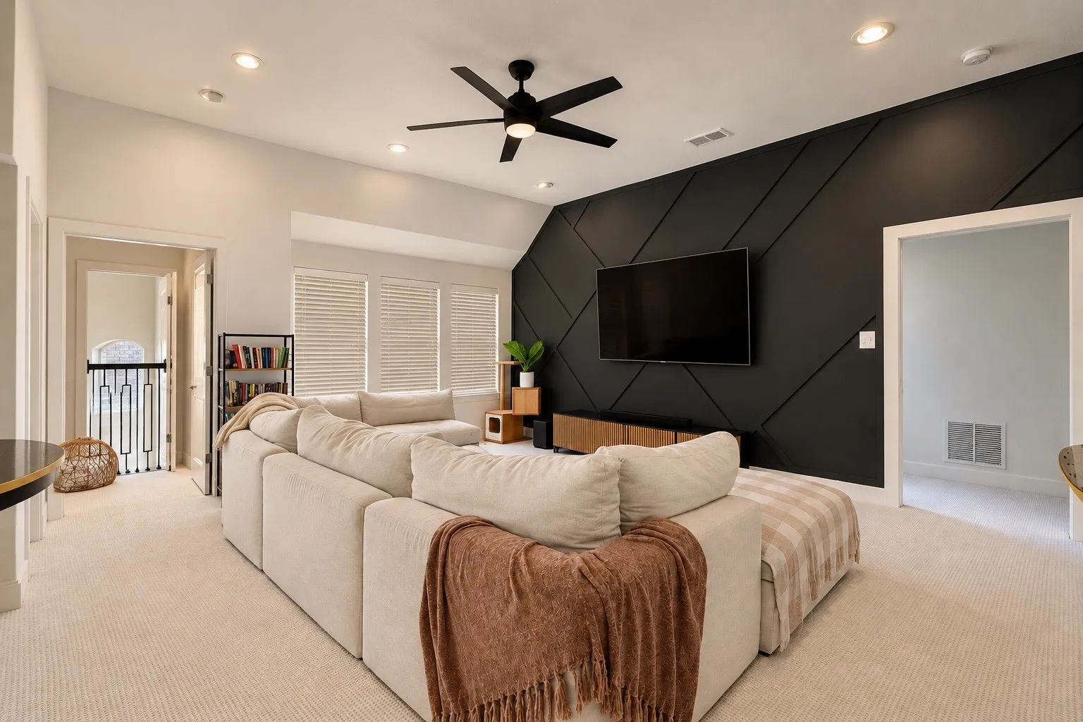 Spacious room featuring vaulted ceilings, recessed lighting, a modern ceiling fan, a striking accent wall with geometric paneling, and multiple windows with horizontal blinds