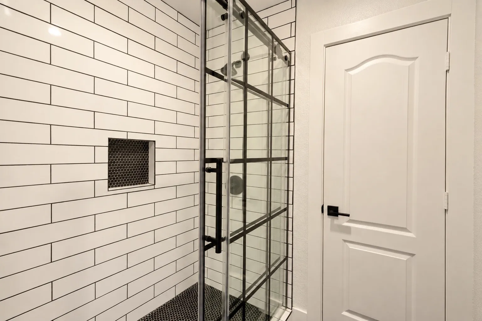 Walk-in shower with subway tile walls, black grid-patterned glass enclosure, and black penny tile shower floor