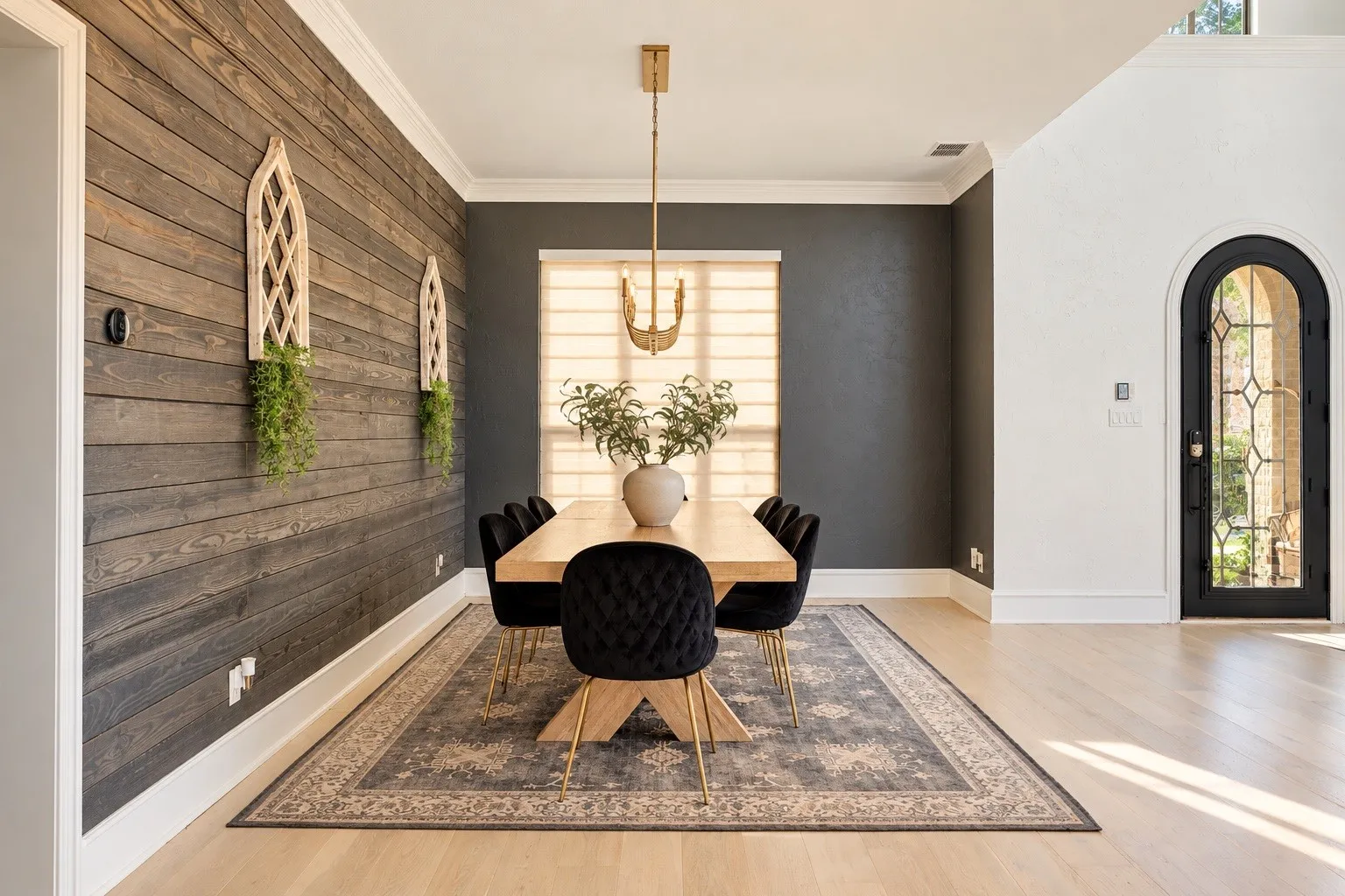 Hardwood flooring, wood-paneled accent wall, arched entryway with decorative glass, and a modern chandelier