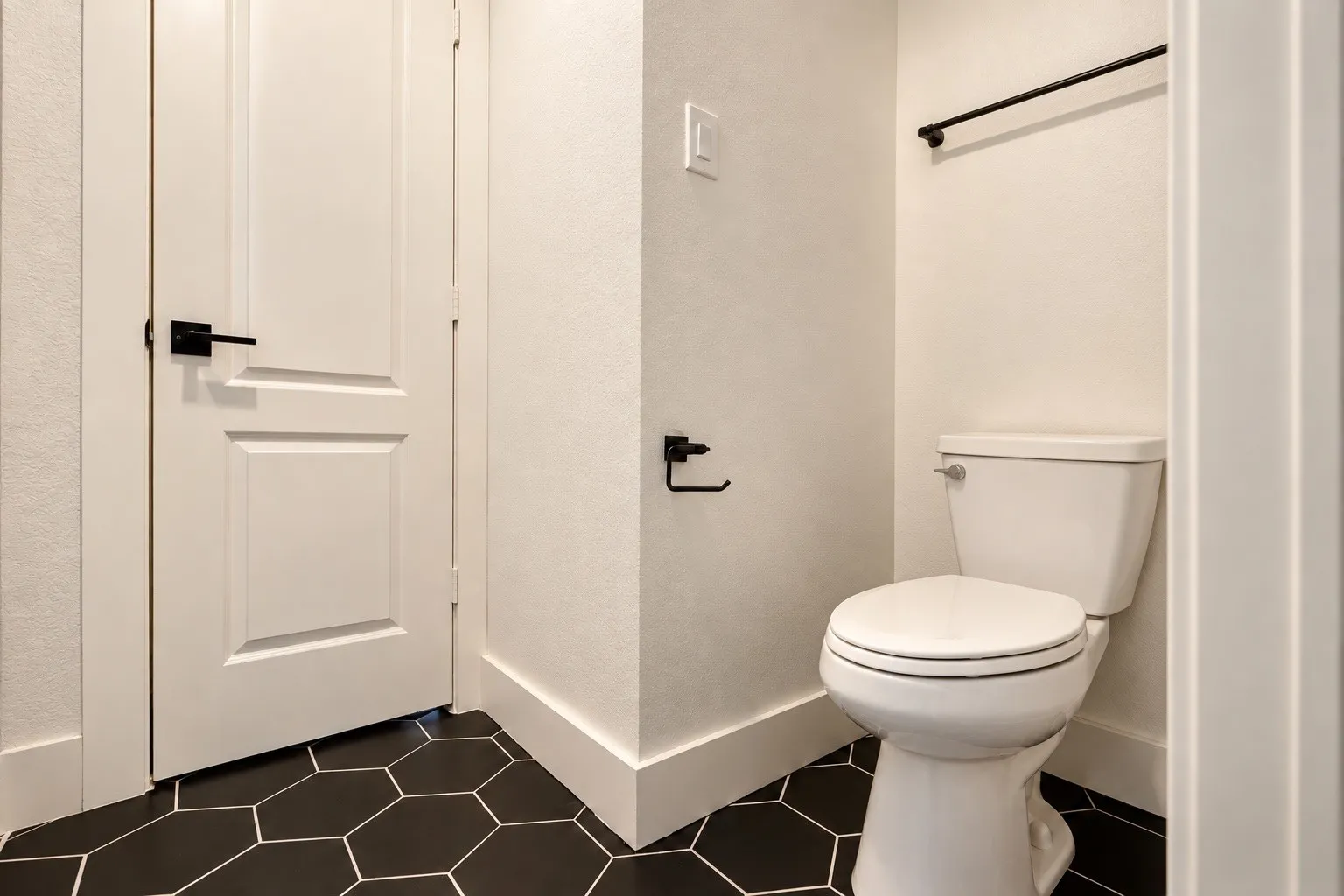 Hexagonal floor tiles, paneled door with matte black hardware, white walls, and a white toilet