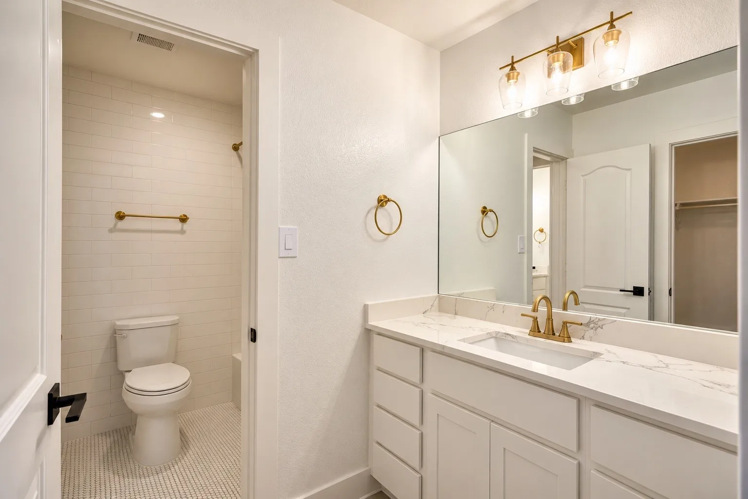 White vanity with a stone-finish countertop, undermount sink, and brass-finish faucet