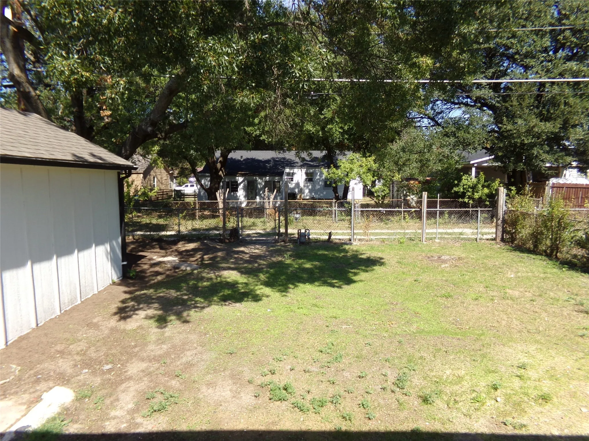 Expansive backyard featuring a partial chain-link fence, mature trees, and a white-sided outbuilding with a shingle roof