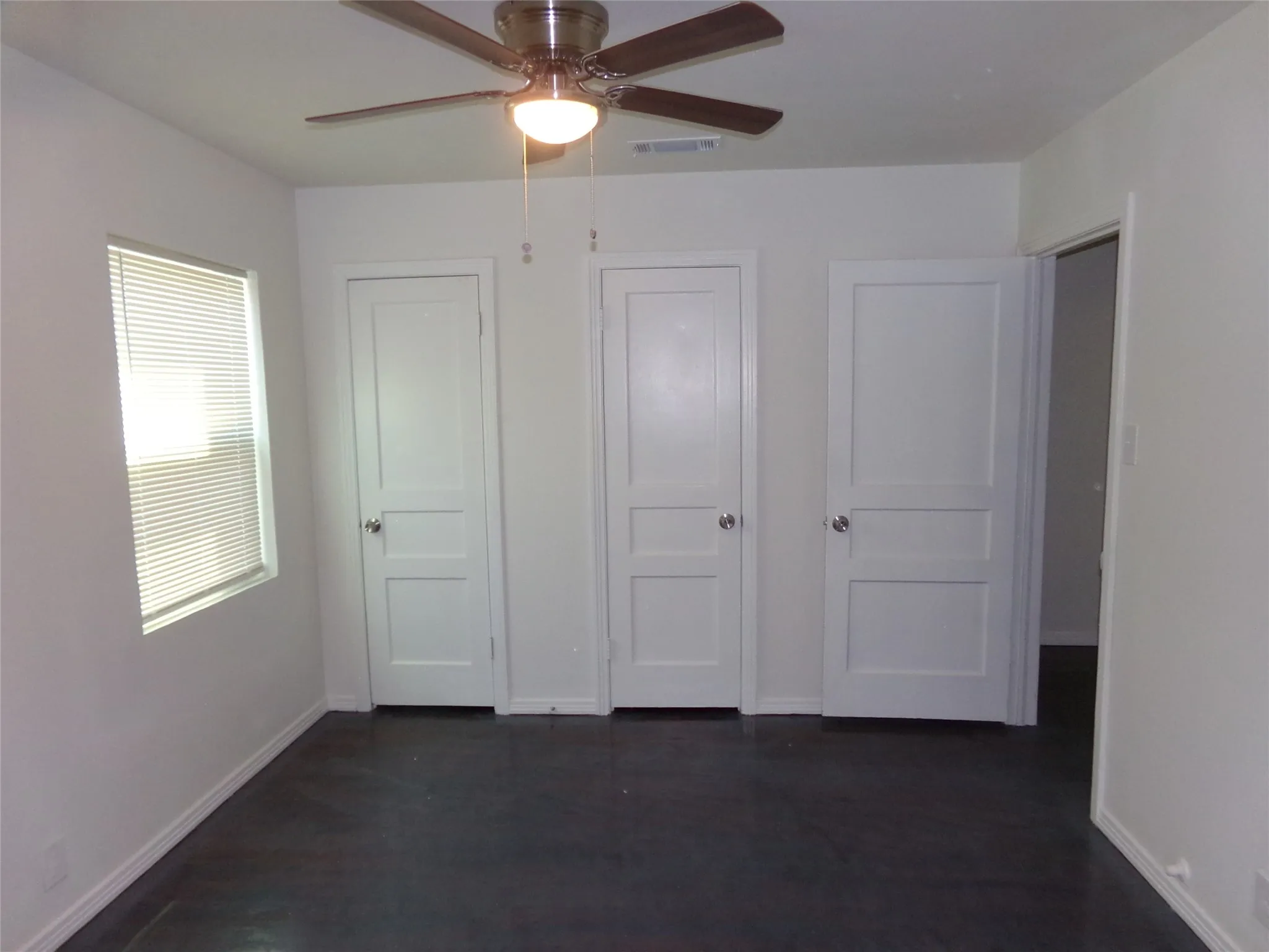 Dark-toned flooring, white walls, and a ceiling fan with light fixture