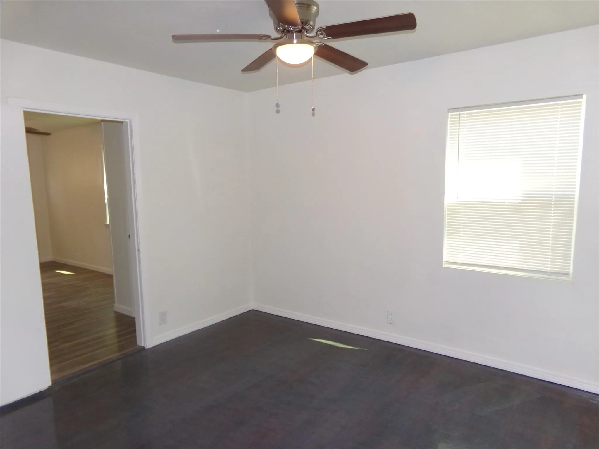 Dark wood-finish flooring, white walls, ceiling fan, and a window with blinds