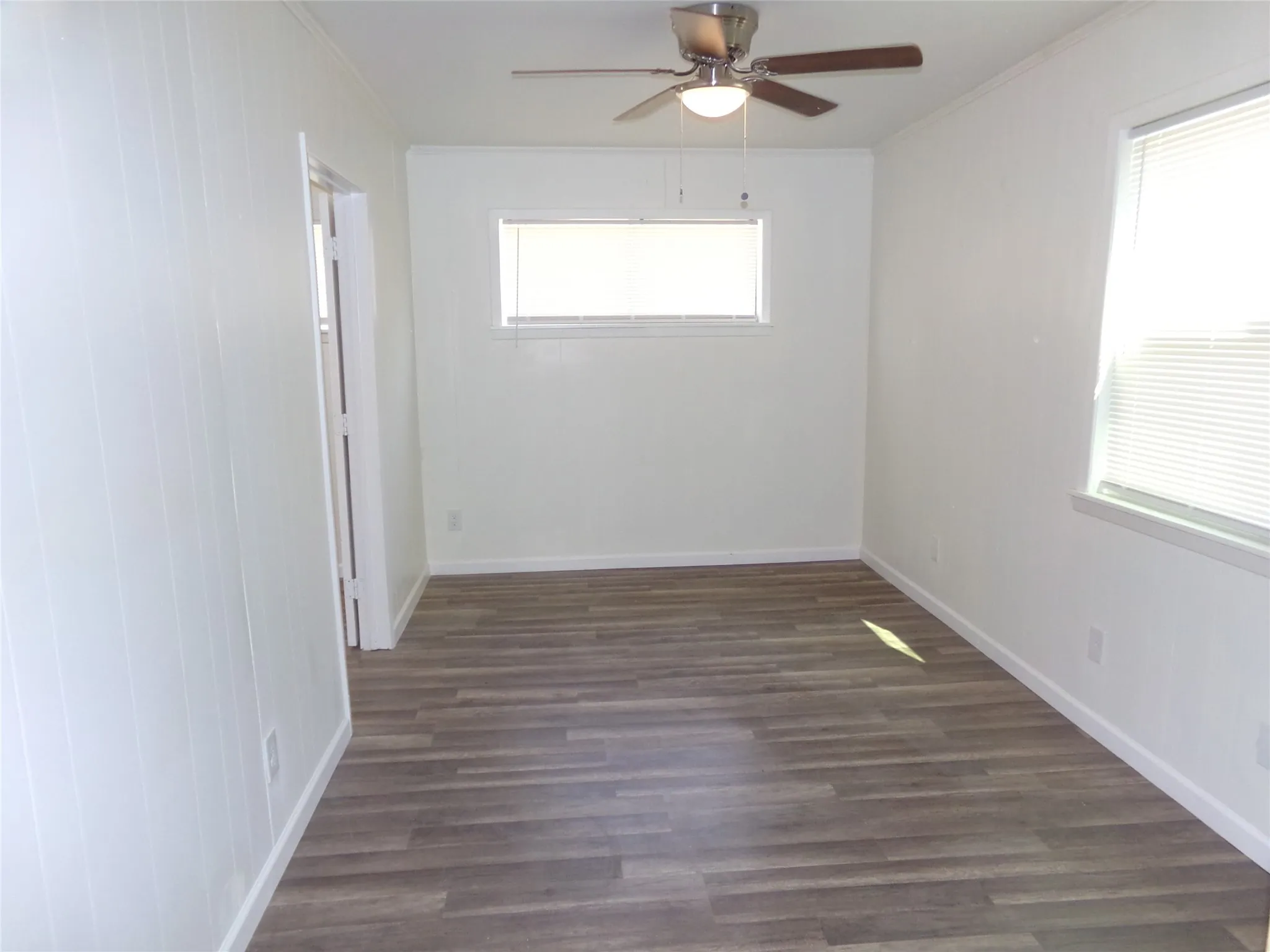 Wood-finish flooring, white paneled wall, dual windows, and ceiling fan with integrated lighting