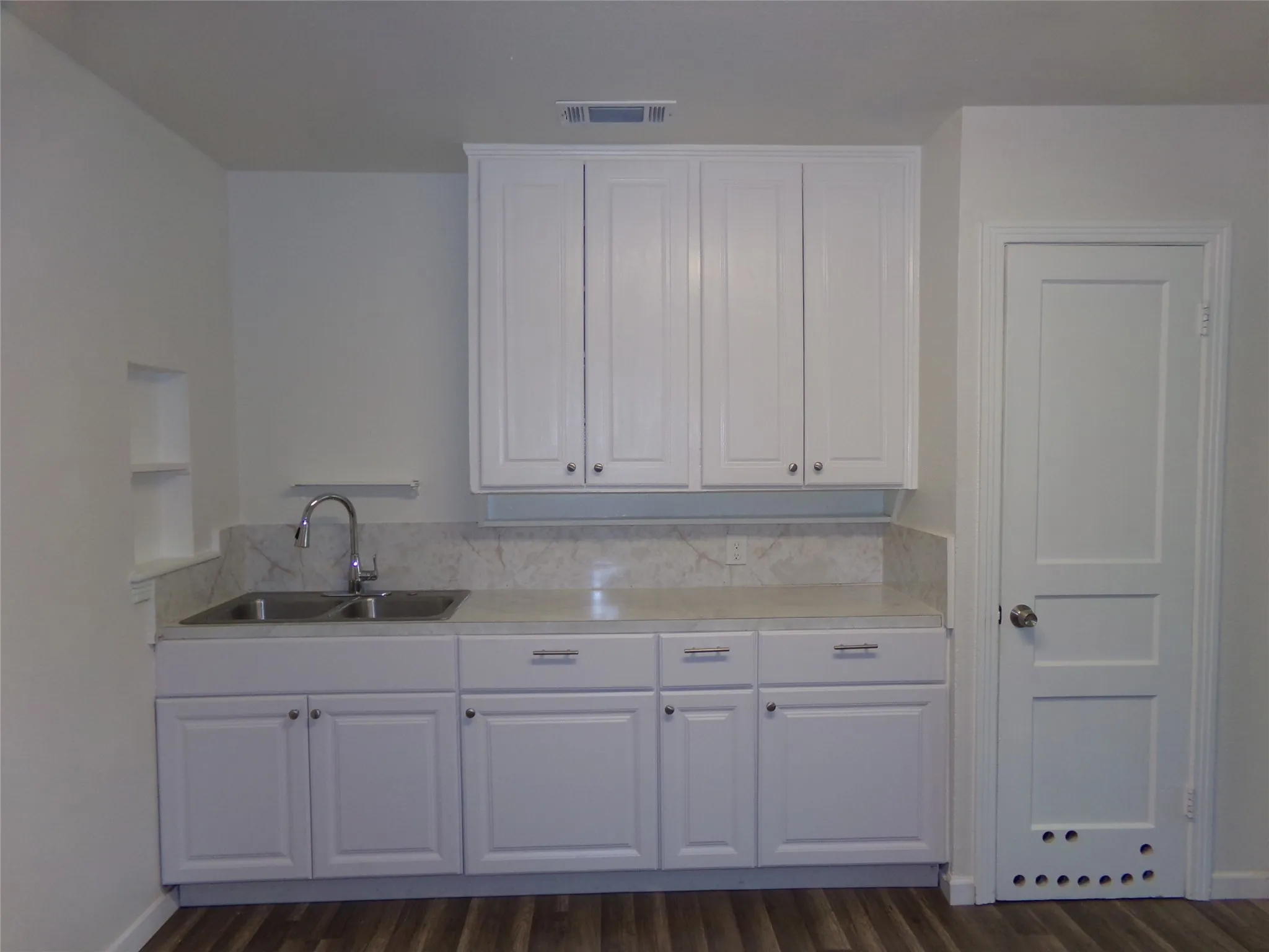 White shaker-style cabinetry with chrome hardware, dual basin stainless steel sink, light-toned countertop, and wood-finish flooring