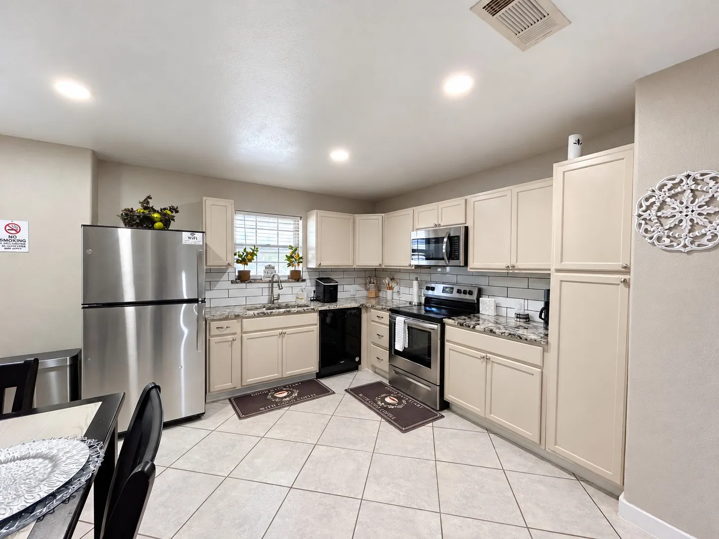 Kitchen featuring stainless steel appliances, light-toned cabinetry, granite-finish countertops, subway tile backsplash, and a tiled floor