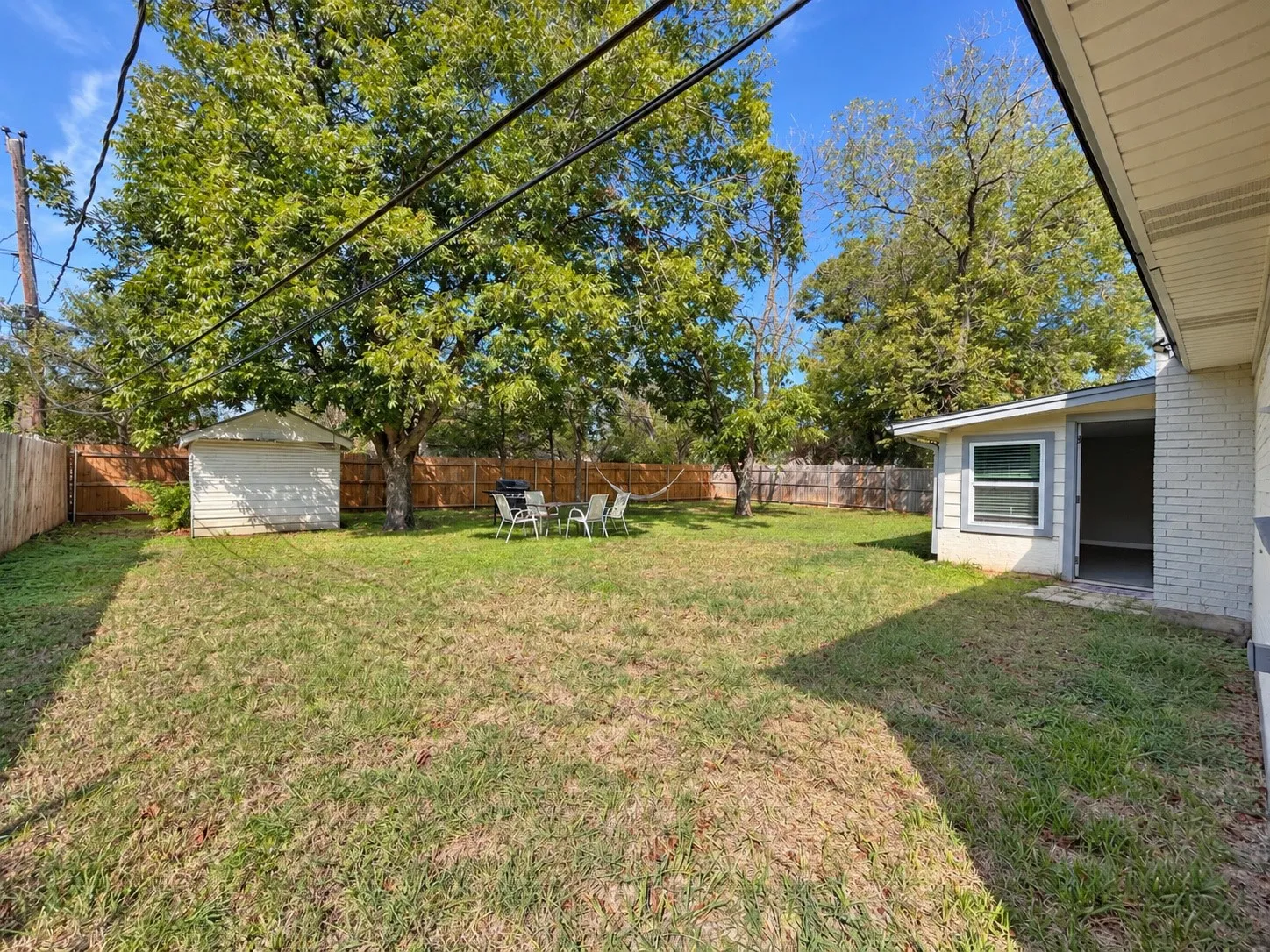 Expansive fenced backyard featuring a storage shed, mature trees, and a ground-level patio