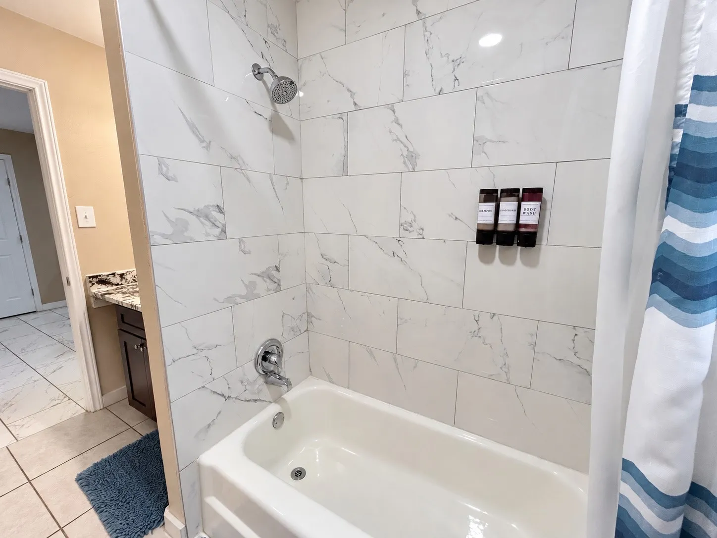 Bathtub with white subway tile surround, chrome fixtures, and a vanity with a dark wood-finish cabinet and granite-style countertop