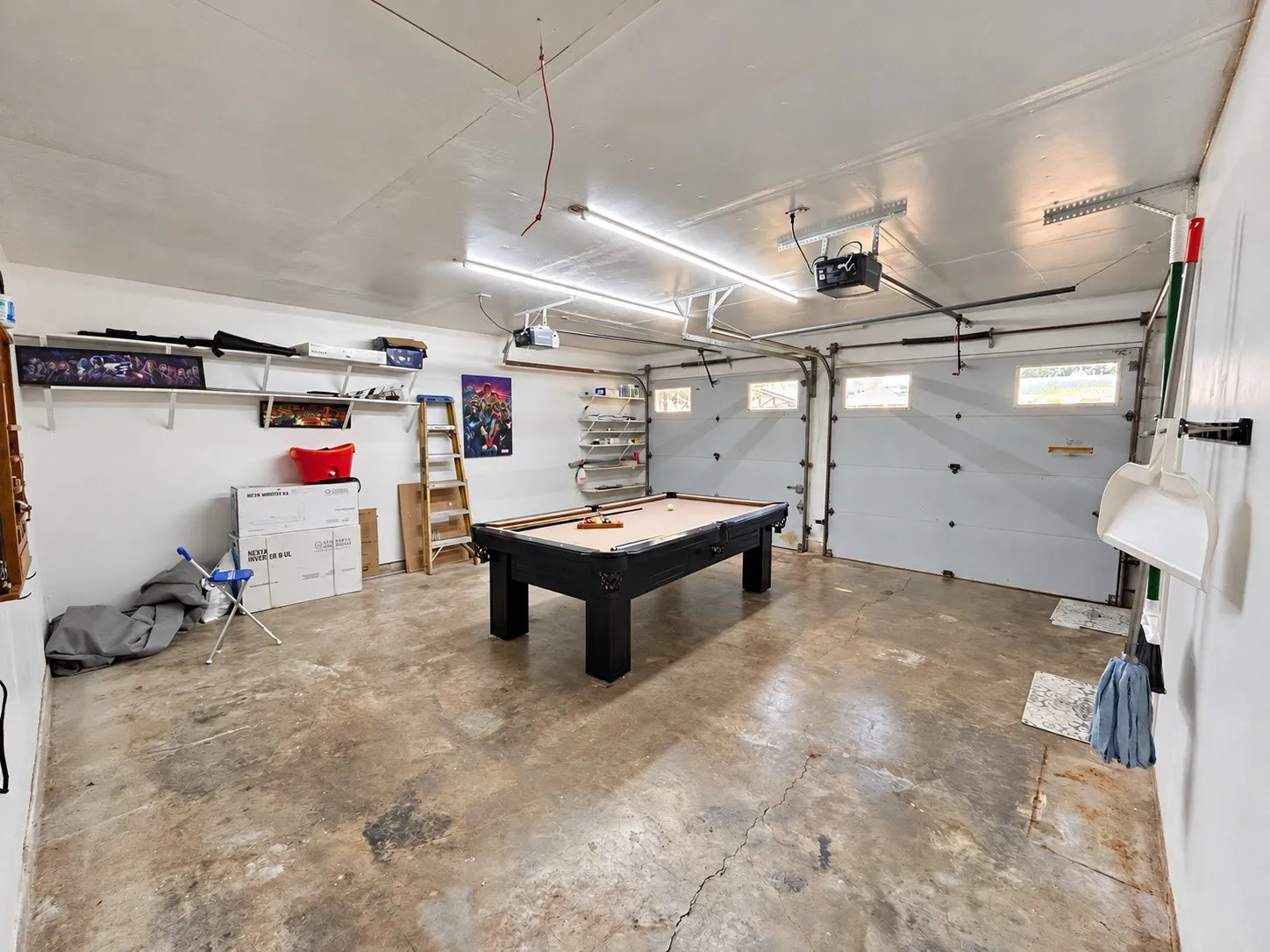 Expansive garage space with concrete flooring, two overhead garage doors with window inserts, and permanent wall shelving