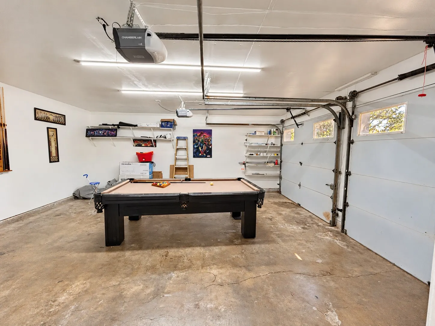 Garage space featuring white walls, overhead lighting, a garage door opener, and built-in shelving